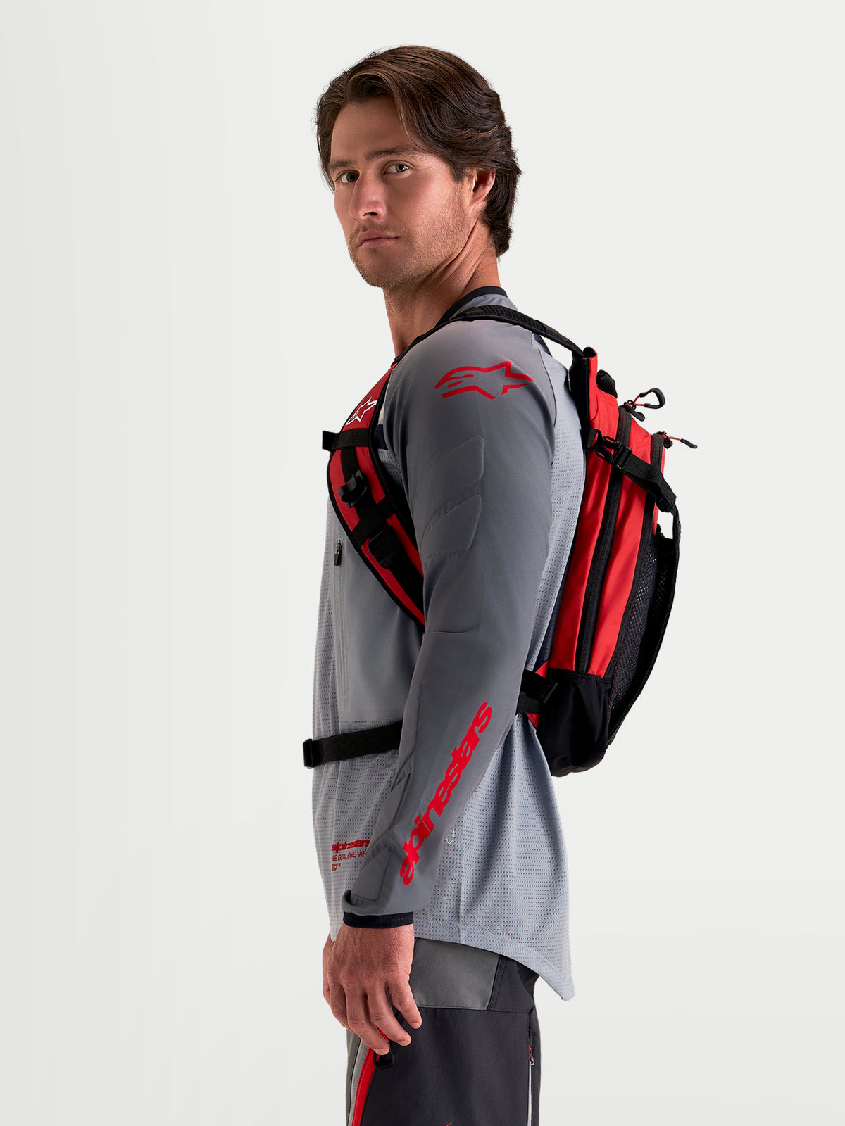 Alpinestars Zaino AT-9, zaino da motocross nero e rosso acceso, vista laterale con profilo indossato da un modello che indossa attrezzatura da MX coordinata, con struttura leggera in tessuto e sistema di imbracatura ergonomico
