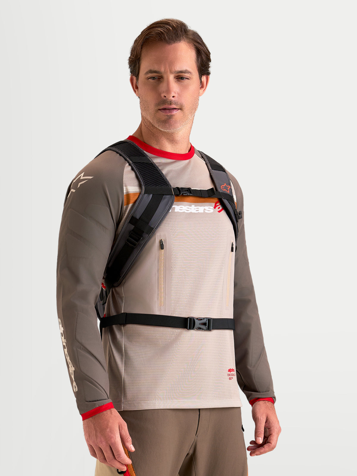 Alpinestars Zaino AT-9, zaino da motocross color marrone noce e grigio scuro, indossato da un modello che mostra gli spallacci imbottiti e il sistema di chiusura con fibbia, struttura in tessuto leggero