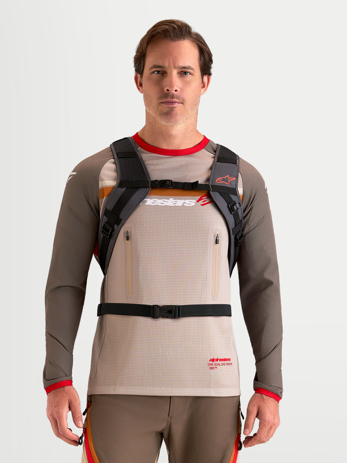 Alpinestars Zaino AT-9, zaino da motocross color marrone noce e grigio scuro, vista frontale di un modello che indossa imbracatura per le spalle imbottita e sistema di cinghie con fibbia