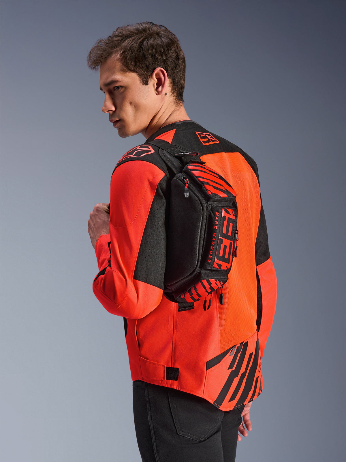 Alpinestars MM93 Waist Bag, marsupio nero con dettagli rosso fluo e rosso brillante, indossato da un modello sulla schiena sopra una giacca da moto rossa e nera, con loghi MM93 e grafiche Marc Marquez