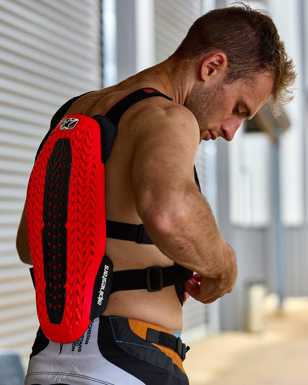 Alpinestars A-5 Plasma Chest Protector, rosso e nero, con paraschiena testurizzato con tecnologia Nucleon PLASMA, indossato da un uomo che regola le cinghie nere, vista laterale che mette in risalto il guscio protettivo e il design flessibile per la guida fuoristrada