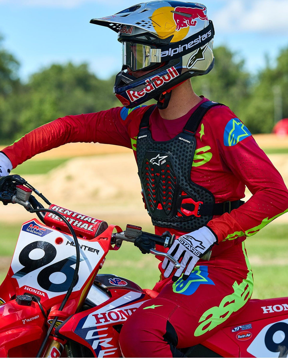 Pilota di motocross con protezione torace Alpinestars A-5 Plasma in nero e rosso, abbinata a maglia e pantaloni da gara rossi e verde lime, seduto su una moto Honda rossa, equipaggiamento protettivo fuoristrada ad alte prestazioni