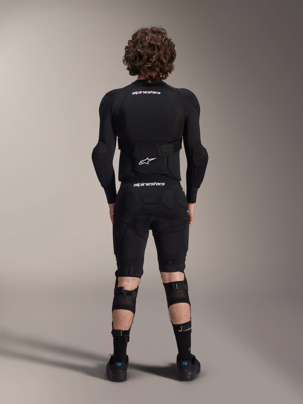 Alpinestars A-Impact Plasma Protection Jacket - Maniche Lunghe, vista posteriore, nera con loghi Alpinestars bianchi, indossata con pantaloncini protettivi e ginocchiere per una protezione completa da mountain bike