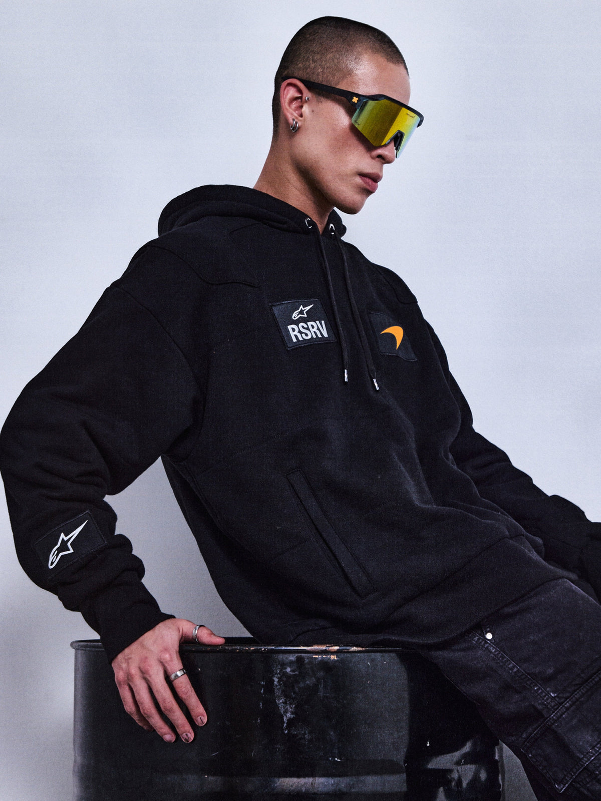 Alpinestars RSRV Rival Hoodie, felpa nera con cappuccio, logo RSRV e patch, stile streetwear premium, unisex, indossata con occhiali da sole riflettenti gialli