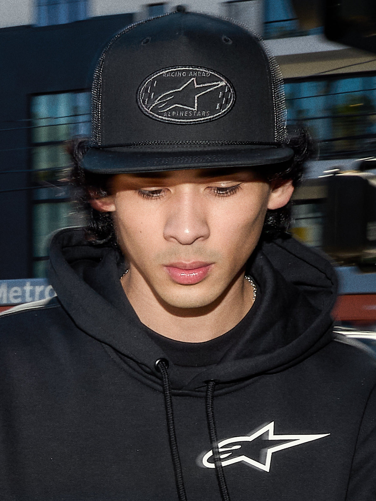 Alpinestars Contender Trucker Hat, berretto lifestyle nero con retro in rete di poliestere, corona strutturata con patch ricamata del logo Astars, indossato da un uomo con felpa nera Alpinestars, streetwear casual ispirato al motorsport