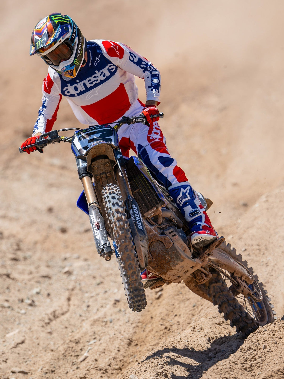 Pilota di motocross in azione su una pista sterrata, indossa la maglia Limited Edition Techstar Fortitude in rosso, bianco e blu, coordinata con pantaloni da gara e stivali abbinati, con logo Alpinestars in evidenza, abbigliamento professionale per gare off-road
