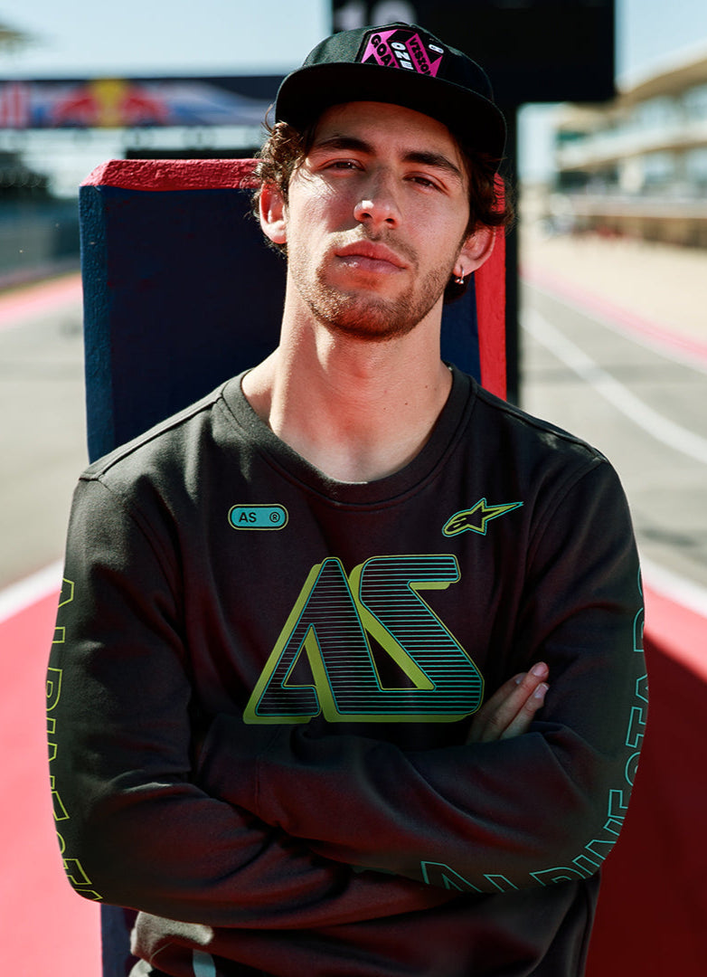 Alpinestars Ayess Csf Tee, maglietta a maniche lunghe, nero, con grafiche AS con sfumatura verde e gialla sul petto e sulle maniche, streetwear casual ispirato al motorsport indossato in un circuito