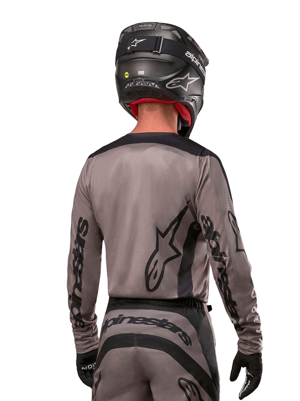 Pilota di motocross visto di spalle che indossa la maglia Alpinestars Fluid Lurv 2024 in Mud Black, con branding Alpinestars nero su maniche e schiena, abbinata a casco nero e attrezzatura per corse fuoristrada