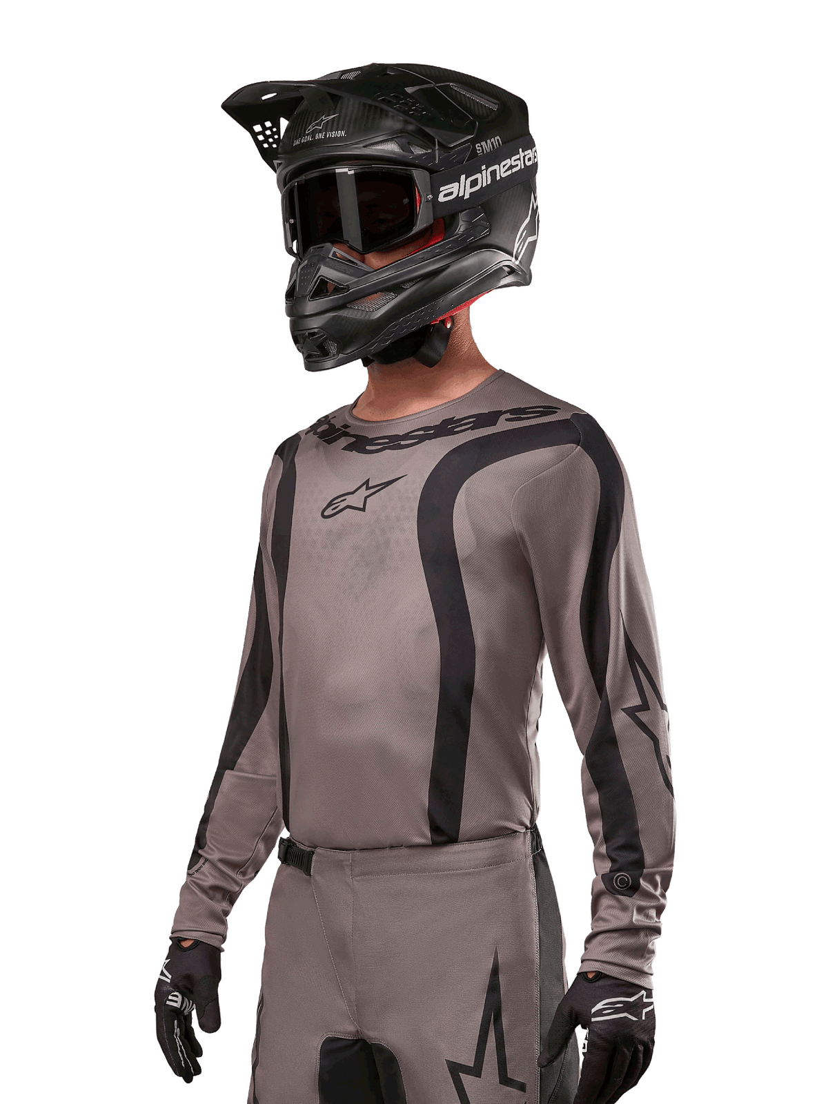 Maglia Alpinestars 2024 Fluid Lurv, maglia da motocross, Mud Black e grigio, design a maniche lunghe con strisce nere curve e loghi, indossata con pantaloni coordinati e un casco da motocross nero, kit da gara fuoristrada coordinato