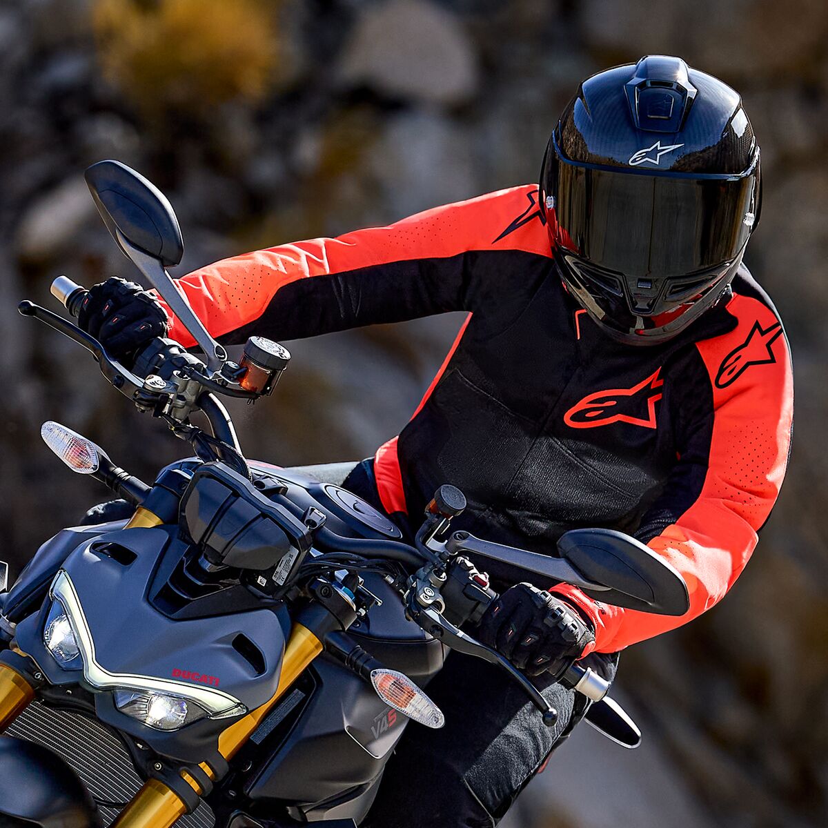 Giacca Alpinestars Viper Air V4, rosso fluo e nero, indossata da un motociclista in piega su una moto sportiva, casco integrale nero e guanti, abbigliamento tecnico racing e sportivo ad alte prestazioni