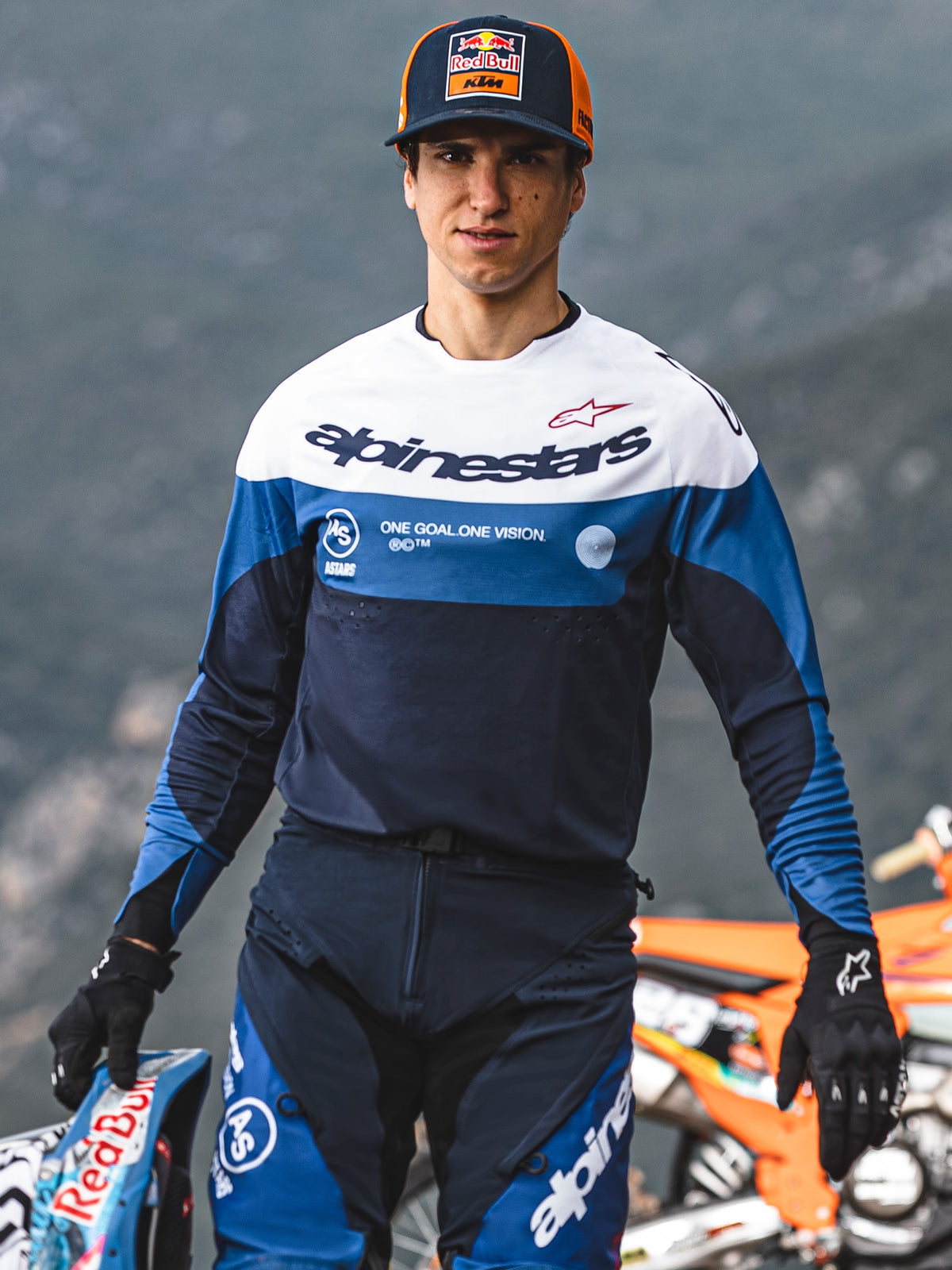 Pilota di motocross con maglia Alpinestars Pro-Dura in Navy, blu brillante e bianco, con il marchio Alpinestars e lo slogan 'One Goal. One Vision.', abbinata a equipaggiamento coordinato e cappellino Red Bull KTM in un'ambientazione all'aperto.