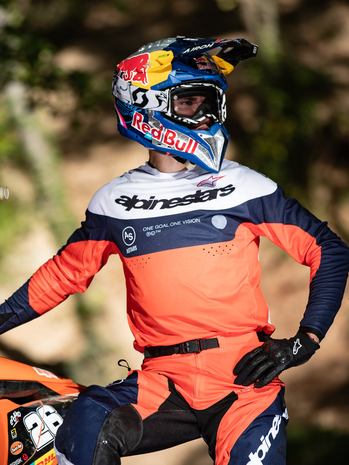 Pilota di motocross con maglia Alpinestars Pro-Dura in Navy, Hot Orange e Bianco, logo sul petto e perforazioni laser, abbinata a casco Red Bull, attrezzatura professionale per prestazioni enduro e off-road.