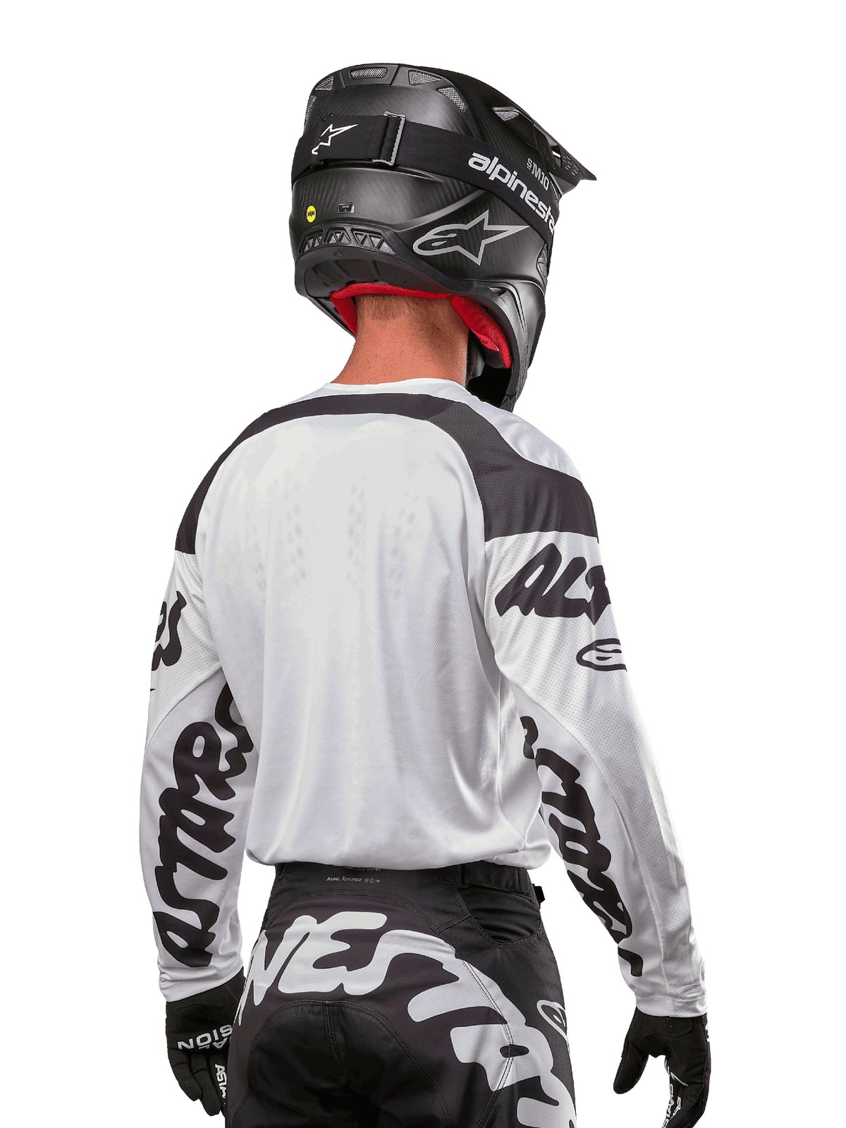 Alpinestars Maglia Racer Hana 2024, bianco e nero, vista posteriore che mostra la vestibilità ergonomica e il branding evidente sulle maniche, abbinata a un casco da motocross nero e pantaloni coordinati bianchi e neri, equipaggiamento da gara ad alte prestazioni per il fuoristrada