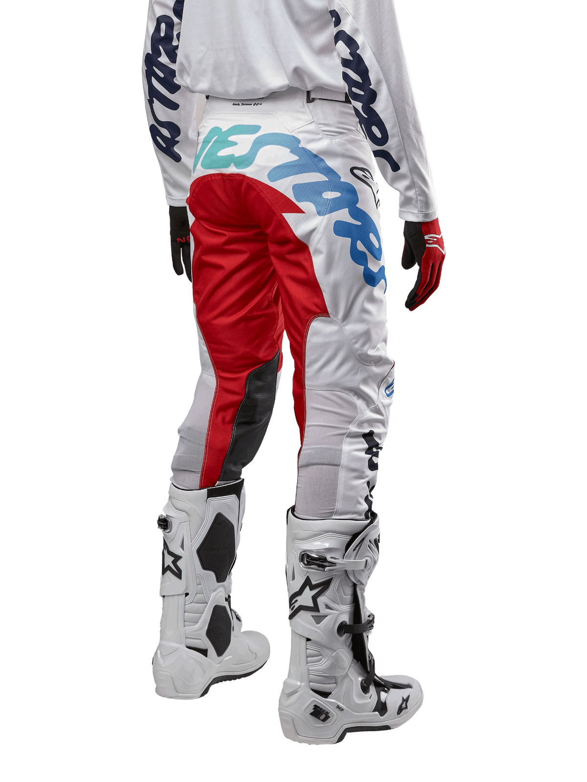 Alpinestars pantaloni Racer Hana 2024, pantaloni da motocross, bianco multicolore con accenti rossi e blu, vista posteriore con grande logo sulla seduta, indossati con stivali da motocross bianchi e neri, progettati per prestazioni e durata fuoristrada
