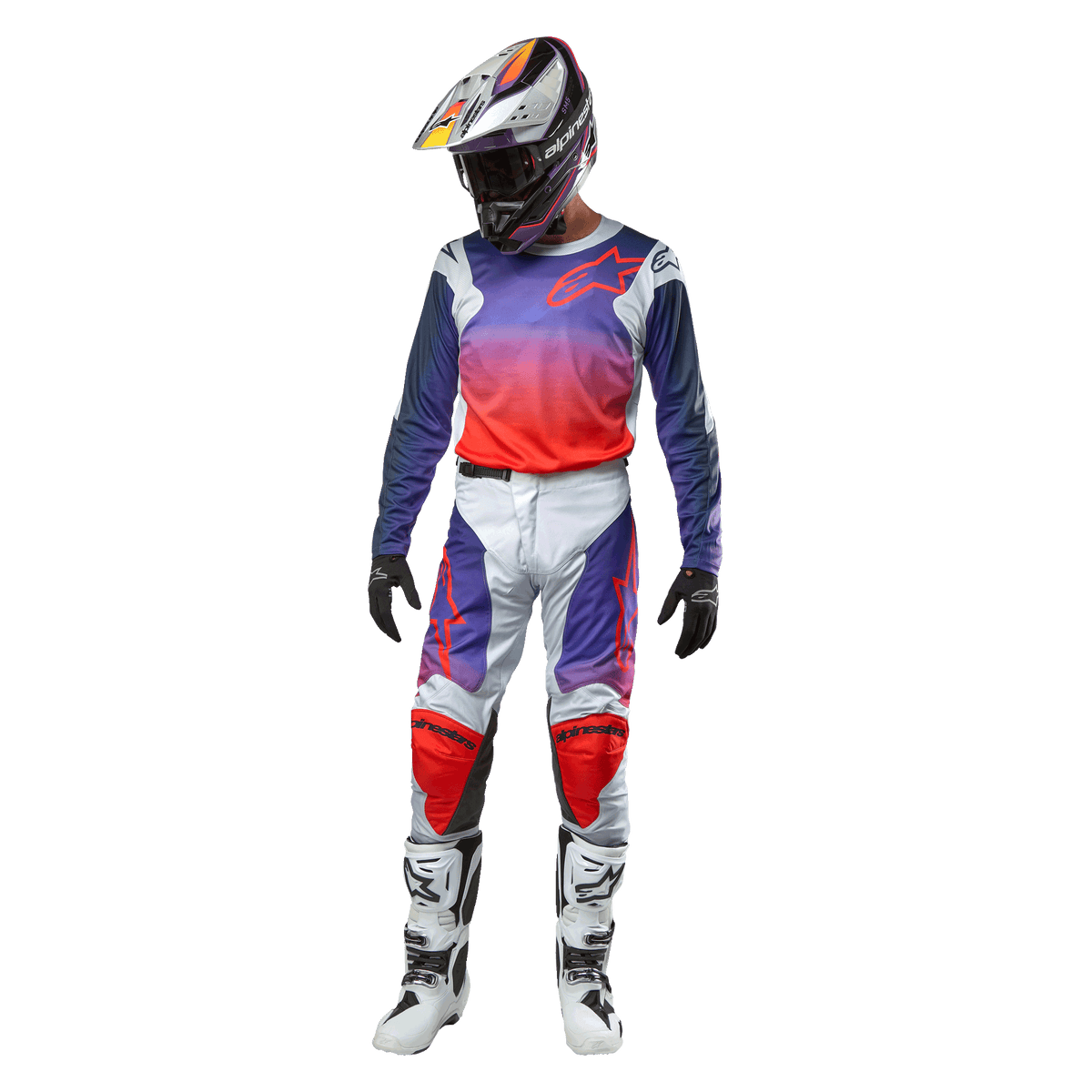 Alpinestars 2024 Racer Hoen Pants, pantaloni da motocross grigio chiaro con accenti arancioni e blu, indossati con maglia sfumata coordinata, casco, guanti neri e stivali bianchi, equipaggiamento protettivo completo