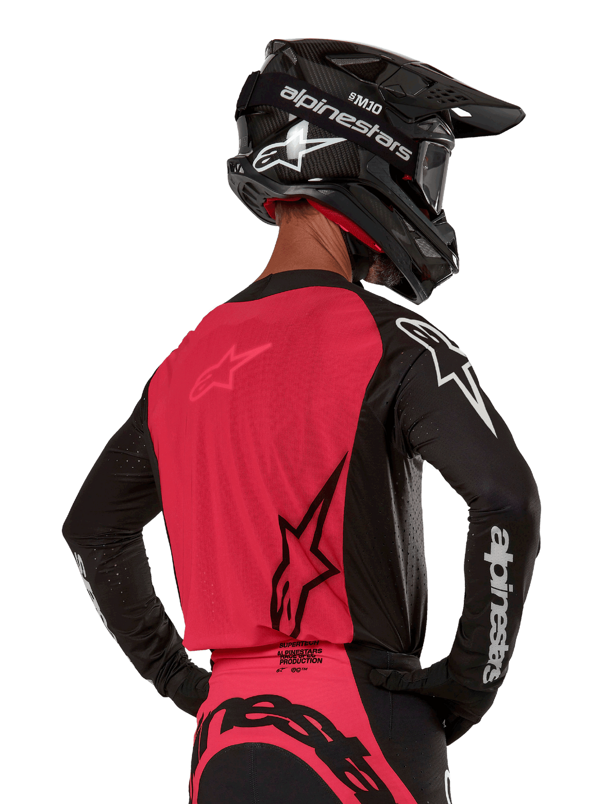 Alpinestars Supertech Ward Jersey 2024, maglia da motocross, nero e rosso berry, vista posteriore con pannello in rete rossa e maniche nere con marchio bianco, indossata con casco in fibra di carbonio nero e guanti, vestibilità race atletica per guida fuoristrada