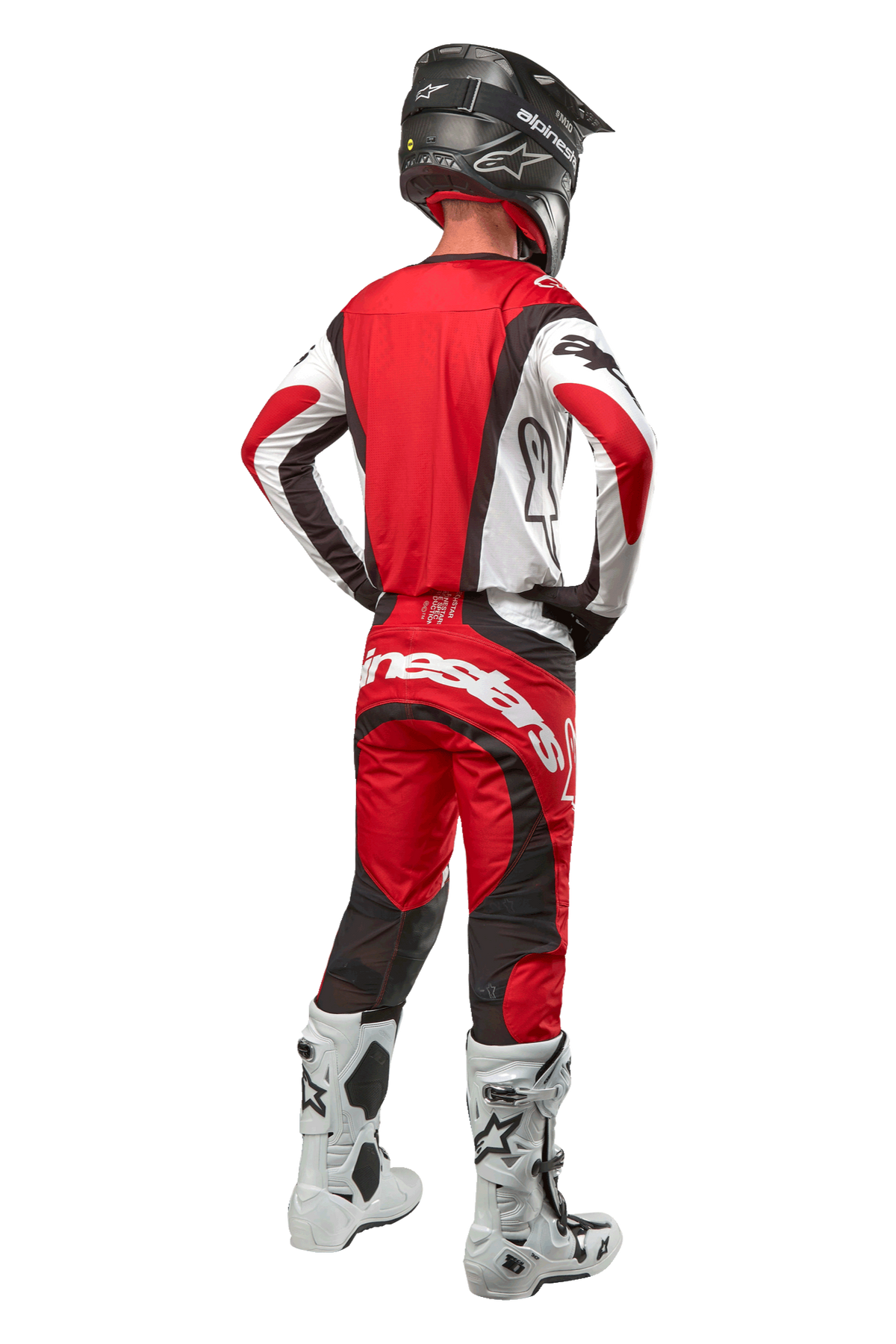 Alpinestars 2024 Techstar Ocuri Pants, pantaloni da motocross, rosso Mars, bianco e nero, vista posteriore di un pilota di motocross con attrezzatura da gara completa, inclusa maglia abbinata, casco nero e stivali bianchi e neri, mette in risalto il marchio Alpinestars e la struttura resistente.