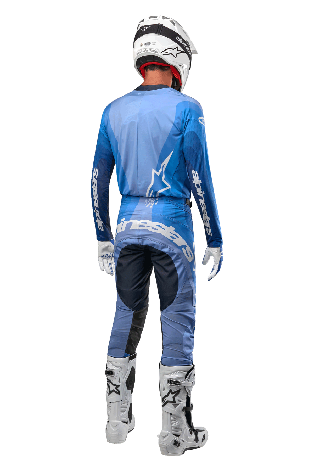 Pilota di motocross visto da dietro con pantaloni Alpinestars Techstar Pneuma 2024 in Dark Navy e azzurro, maglia blu coordinata, casco, guanti e stivali bianchi, con logo Alpinestars su seduta e maniche.