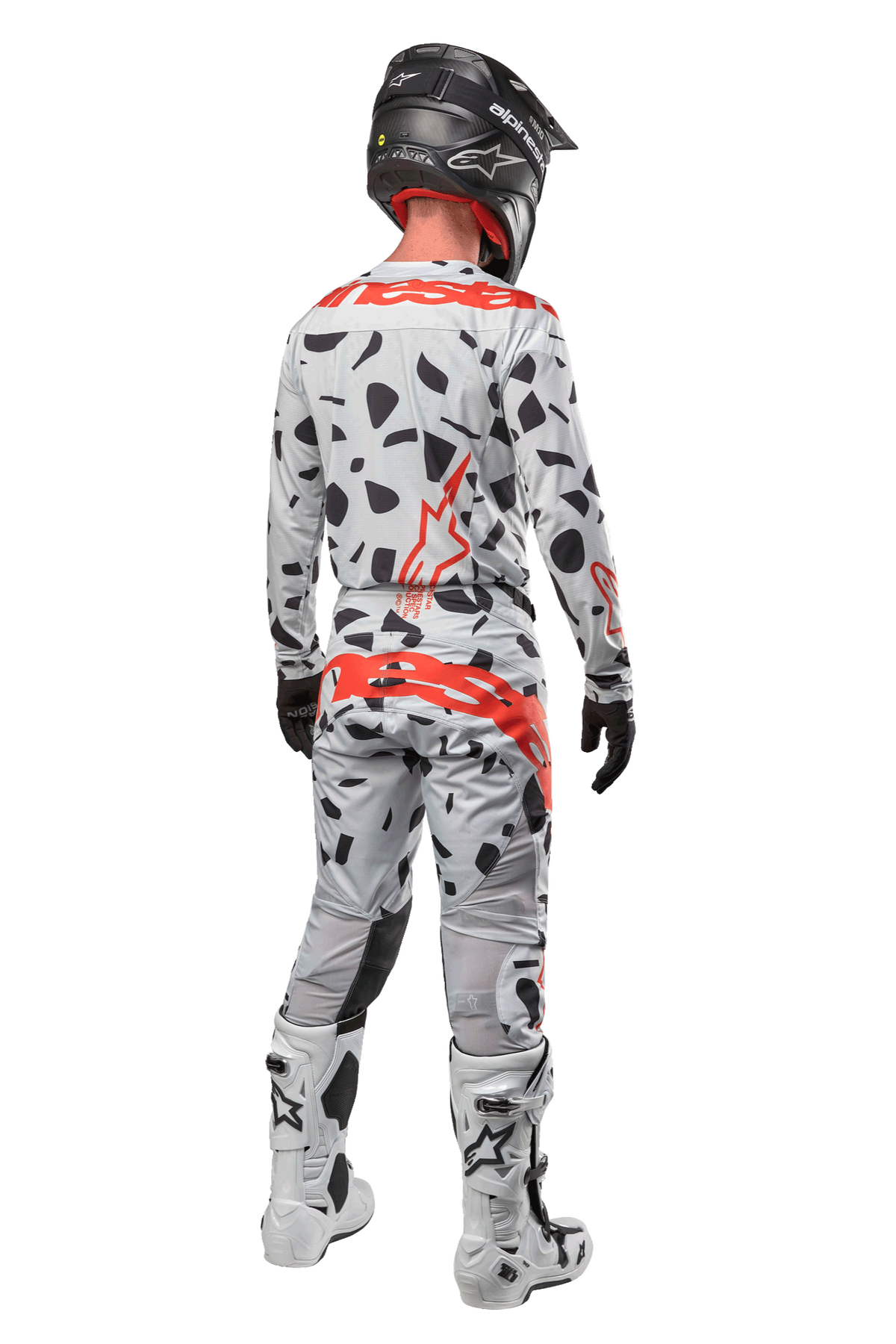 Pilota di motocross visto da dietro, indossa pantaloni Alpinestars 2024 Techstar Rantera, Haze Gray Camo con macchie nere e loghi rossi, maglia coordinata, casco nero e stivali bianchi, completo da gara fuoristrada