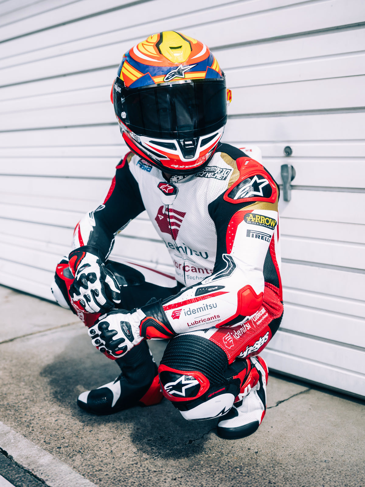 Alpinestars Casco S-R7 Taiyo Furusato, casco integrale da moto racing, rosso, bianco, blu e giallo fluo, certificato ECE 22.06, indossato da un pilota con tuta da corsa in pelle e visiera oscurata.