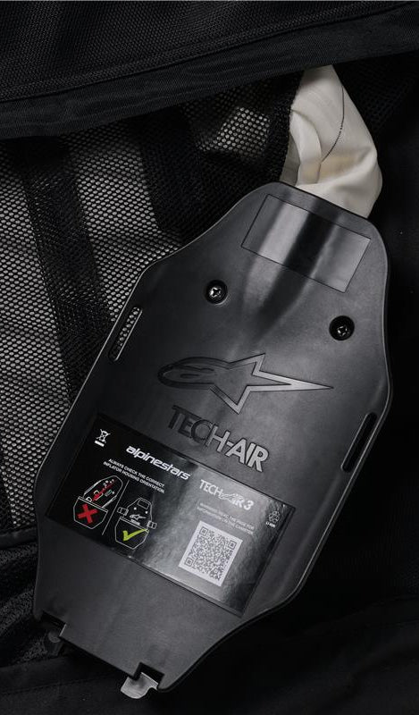 Alpinestars Tech-Air 3 V2 System, vista interna dell'alloggiamento dell'inflatore a gas e della centralina ECU, plastica nera con logo in rilievo, etichetta di sicurezza con codice QR e diagrammi di installazione, fodera interna in rete nera, dettaglio del sistema airbag autonomo riparabile dall'utente