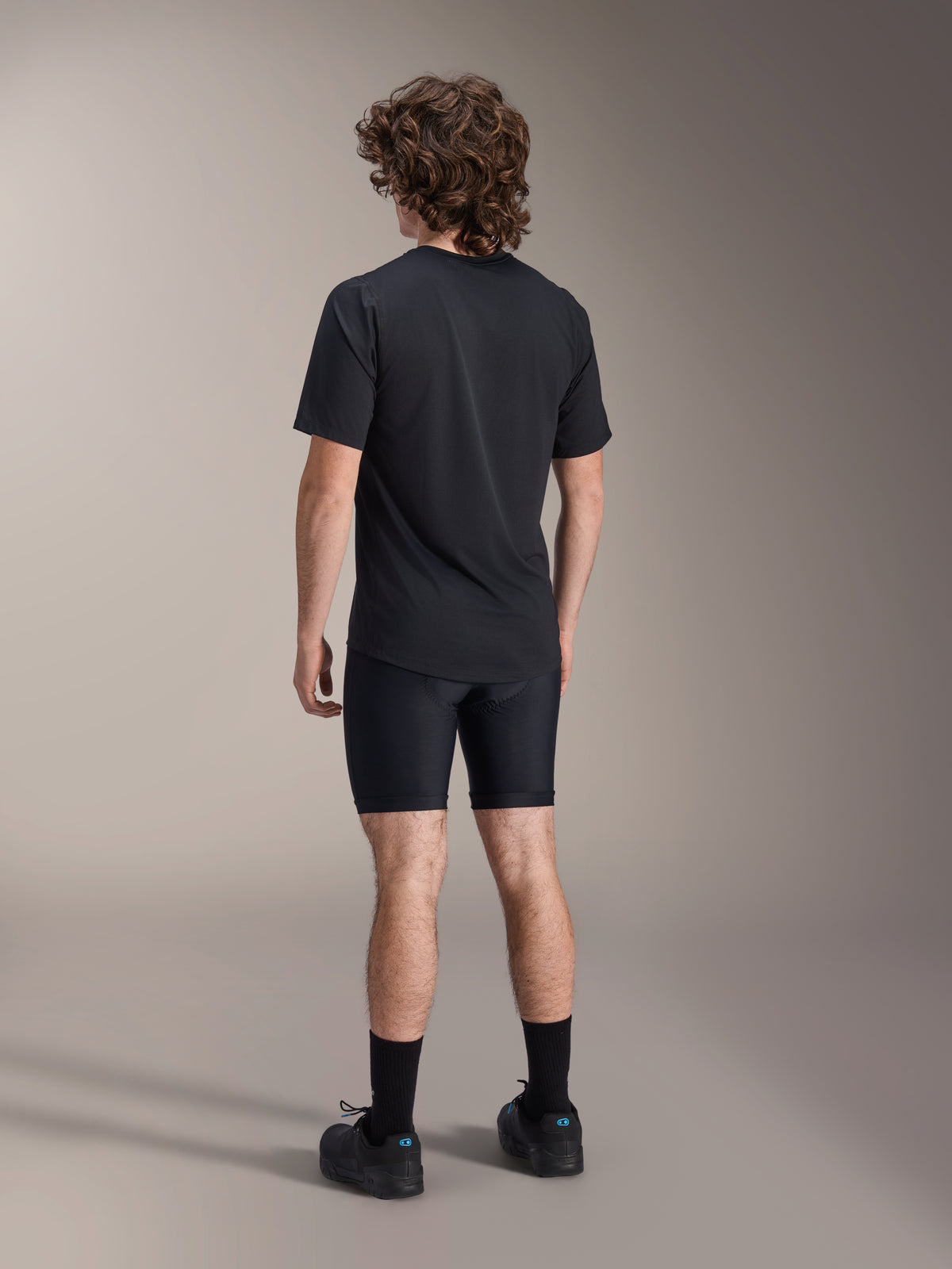 Alpinestars A-Dura Liner Shorts, pantaloncini liner da ciclismo neri, vista posteriore su modello, tessuto elasticizzato aderente con cuciture visibili del fondello, abbinati a una t-shirt nera e scarpe da ciclismo, abbigliamento per mountain bike