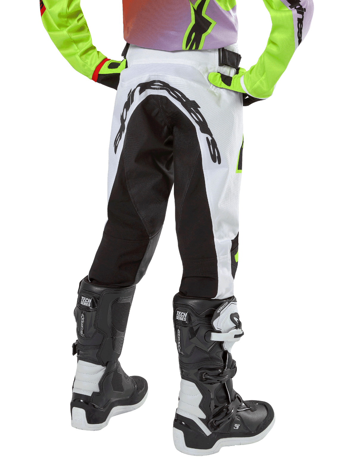 Alpinestars pantaloni Youth Racer Lucent 2024, pantaloni da motocross, bianco e nero con accenti neon, vista posteriore con ampio pannello elasticizzato e logo Alpinestars, indossati con stivali Alpinestars Tech Series bianchi e neri