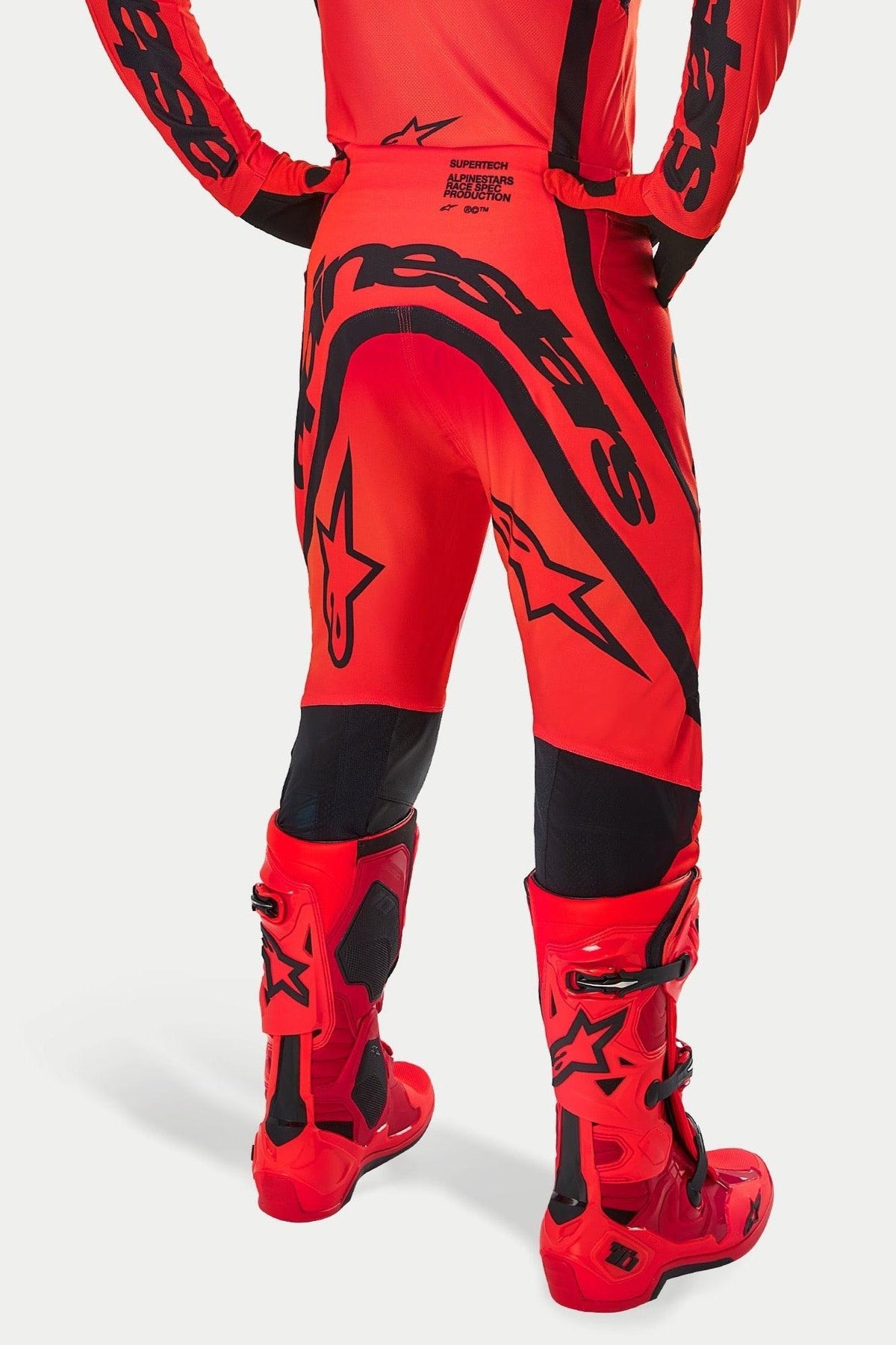 Pantaloni Alpinestars Supertech Ember LE, pantaloni da motocross, rosso fluo, rosso acceso e nero, vista posteriore con grande marchio nero sulla seduta e loghi a stella, indossati con stivali da motocross rossi coordinati, abbigliamento da gara professionale per prestazioni fuoristrada
