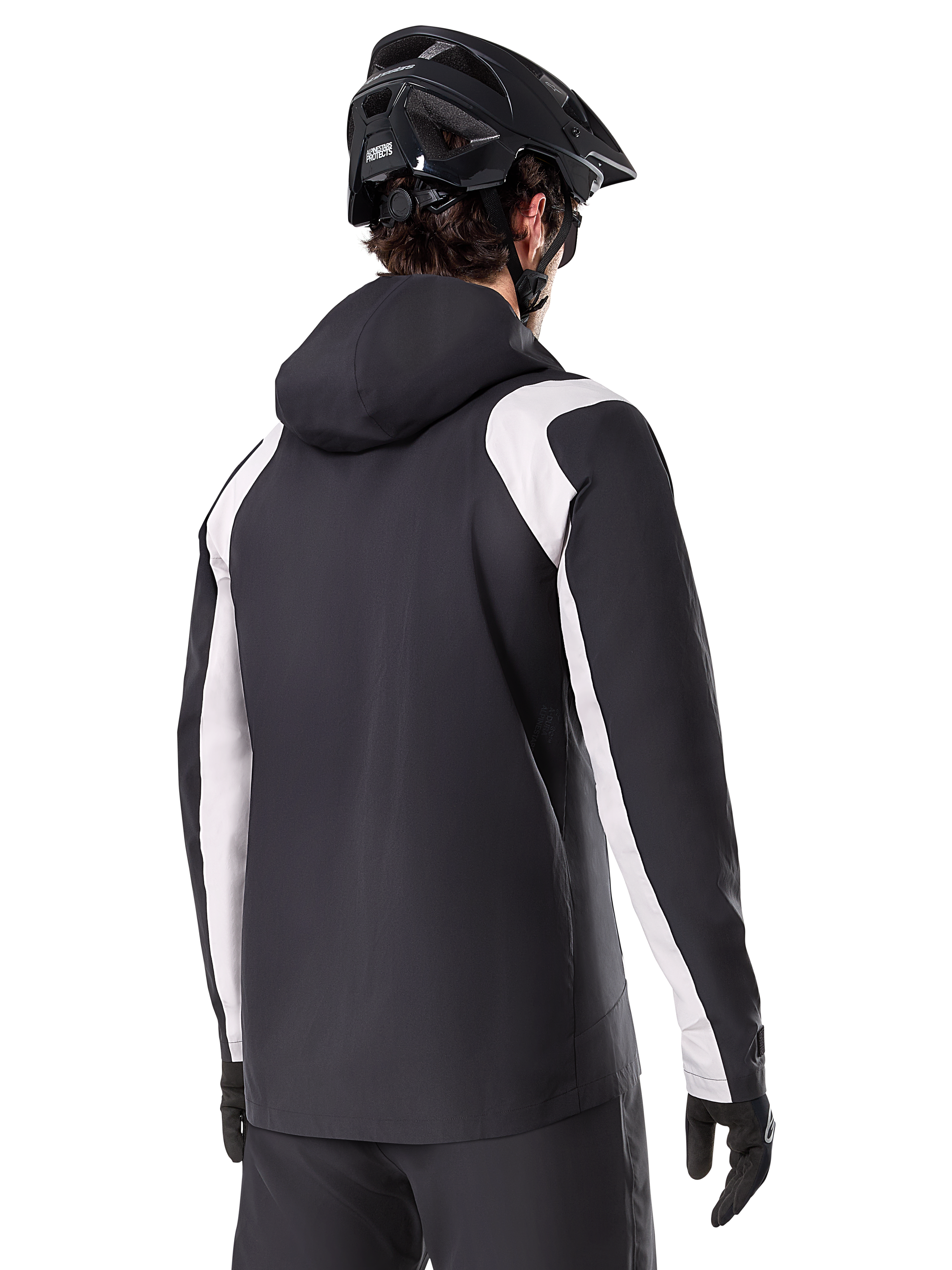 Alpinestars Giacca Antipioggia A-Dura, giacca antipioggia da mountain bike, nera con pannelli bianchi sulle maniche, vista posteriore del ciclista con casco da MTB nero e guanti, costruzione tecnica impermeabile a 2,5 strati, abbigliamento da mountain bike