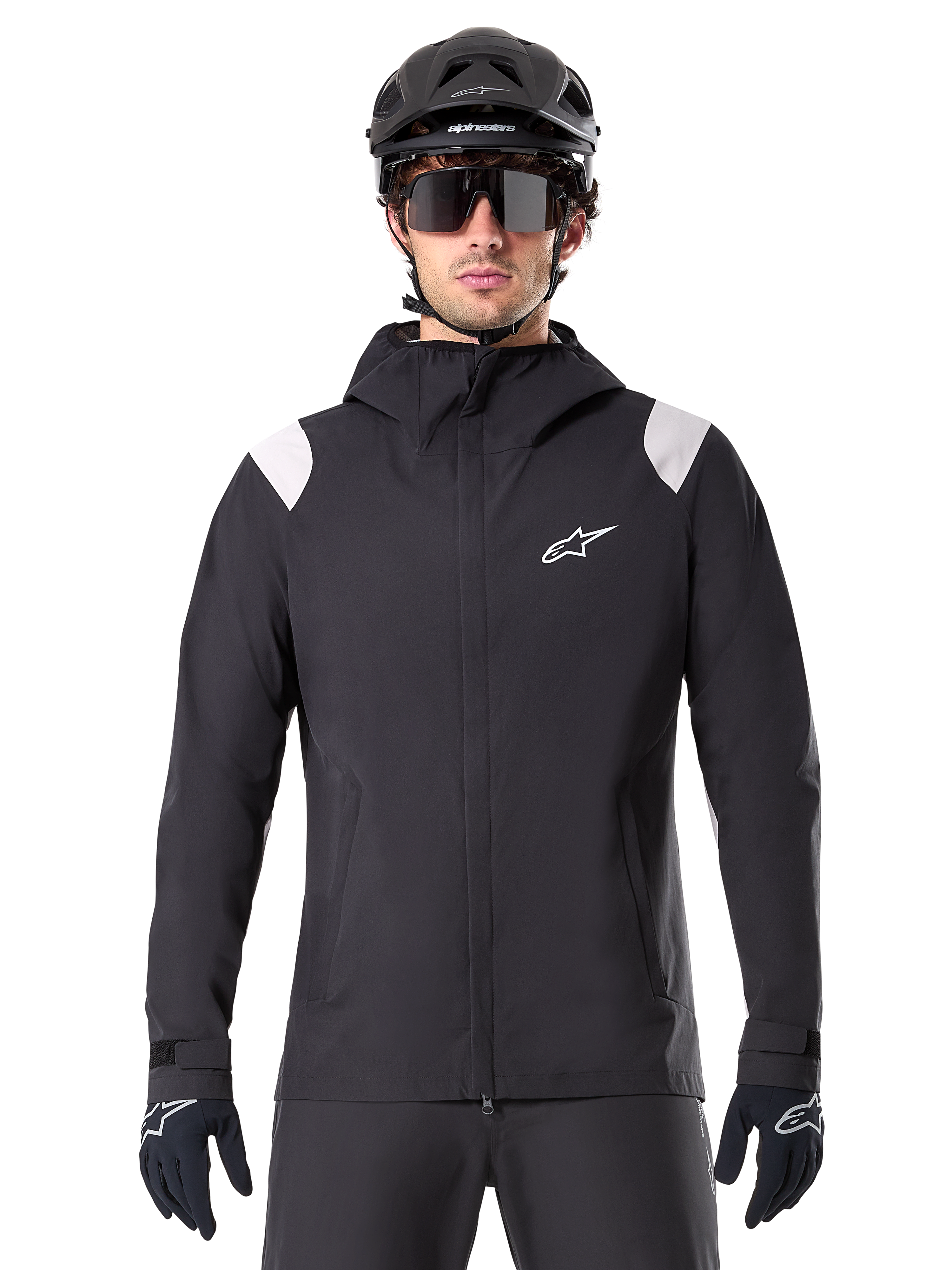 Alpinestars A-Dura Rain Jacket, giacca antipioggia MTB, nero con pannelli bianchi sulle spalle, indossata con casco MTB nero, occhiali da sole e guanti, design impermeabile con cappuccio e cerniera frontale, abbigliamento sportivo outdoor per il ciclismo