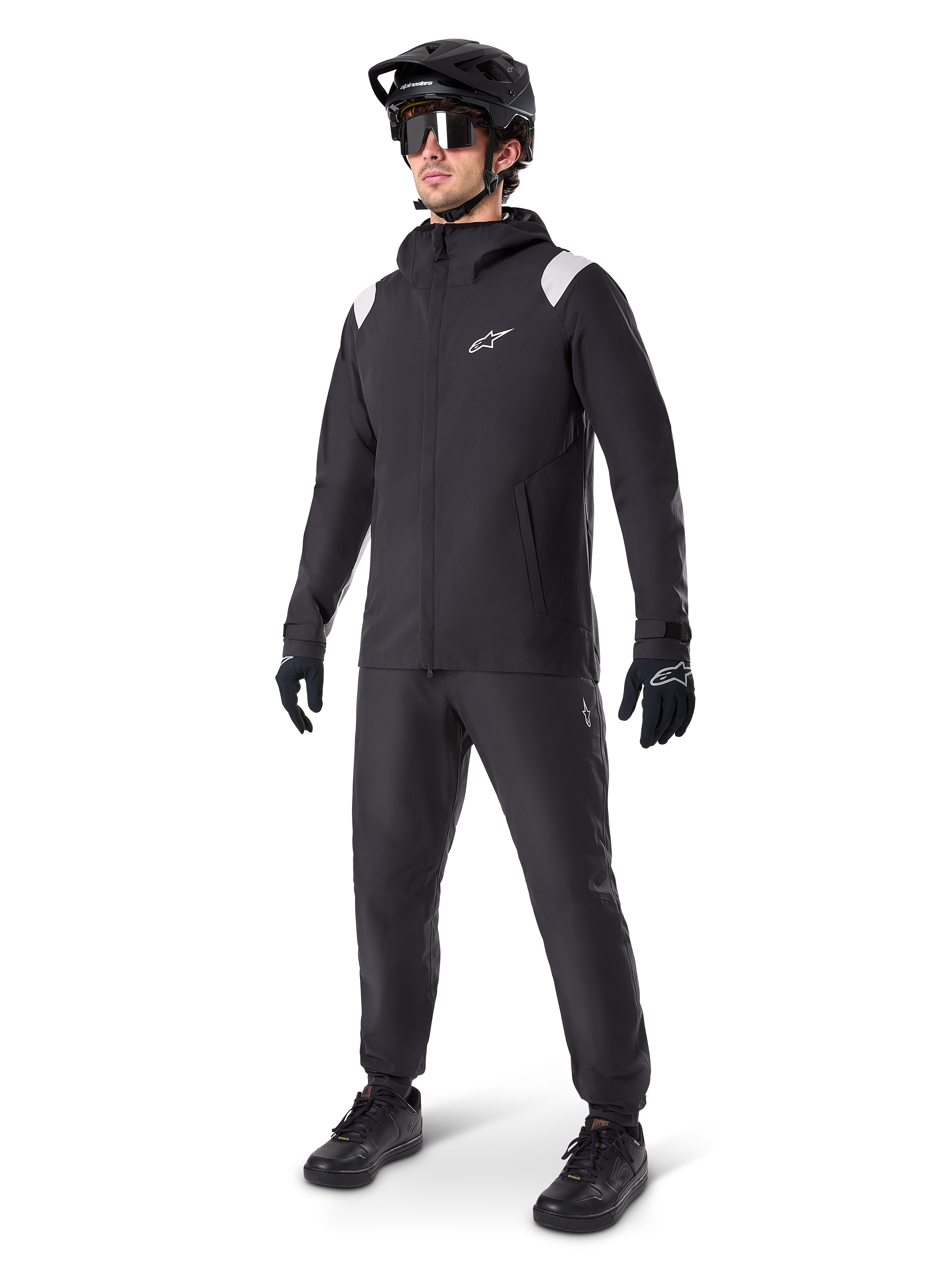 Alpinestars A-Dura Rain Jacket, giacca antipioggia da mountain bike nera, con accenti bianchi sulle spalle, indossata da un ciclista con casco da MTB, occhiali da sole, guanti e pantaloni neri coordinati, abbigliamento tecnico da ciclismo per ogni condizione meteo