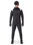 Giacca Antipioggia Alpinestars A-Dura, giacca antipioggia da mountain bike, nera con accenti bianchi sulle spalle e logo bianco sul petto, indossata con pantaloni neri, casco nero, occhiali da sole e guanti, abbigliamento coordinato da mountain bike per il maltempo