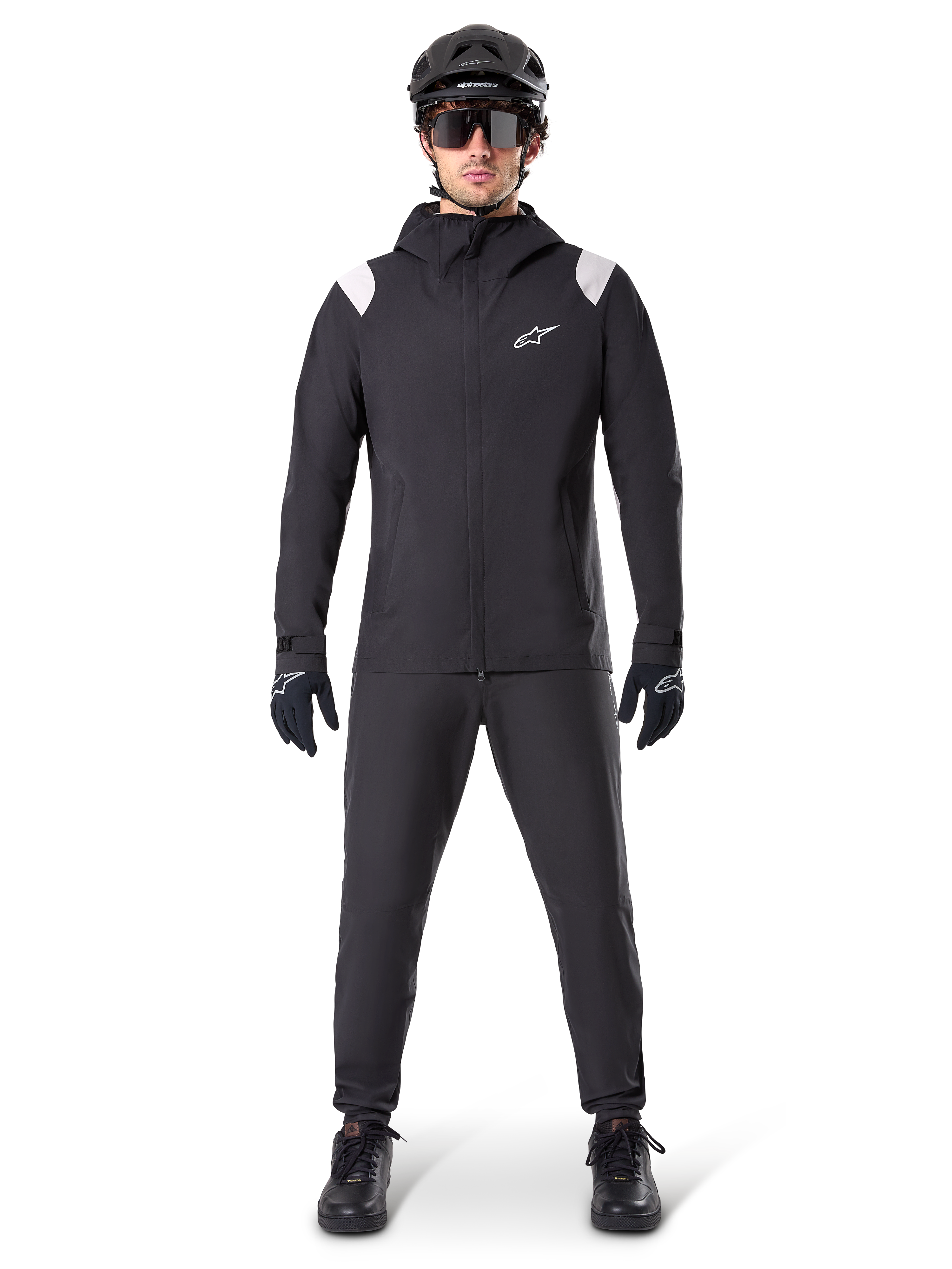 Giacca Antipioggia Alpinestars A-Dura, giacca antipioggia da mountain bike, nera con accenti bianchi sulle spalle e logo bianco sul petto, indossata con pantaloni neri, casco nero, occhiali da sole e guanti, abbigliamento coordinato da mountain bike per il maltempo