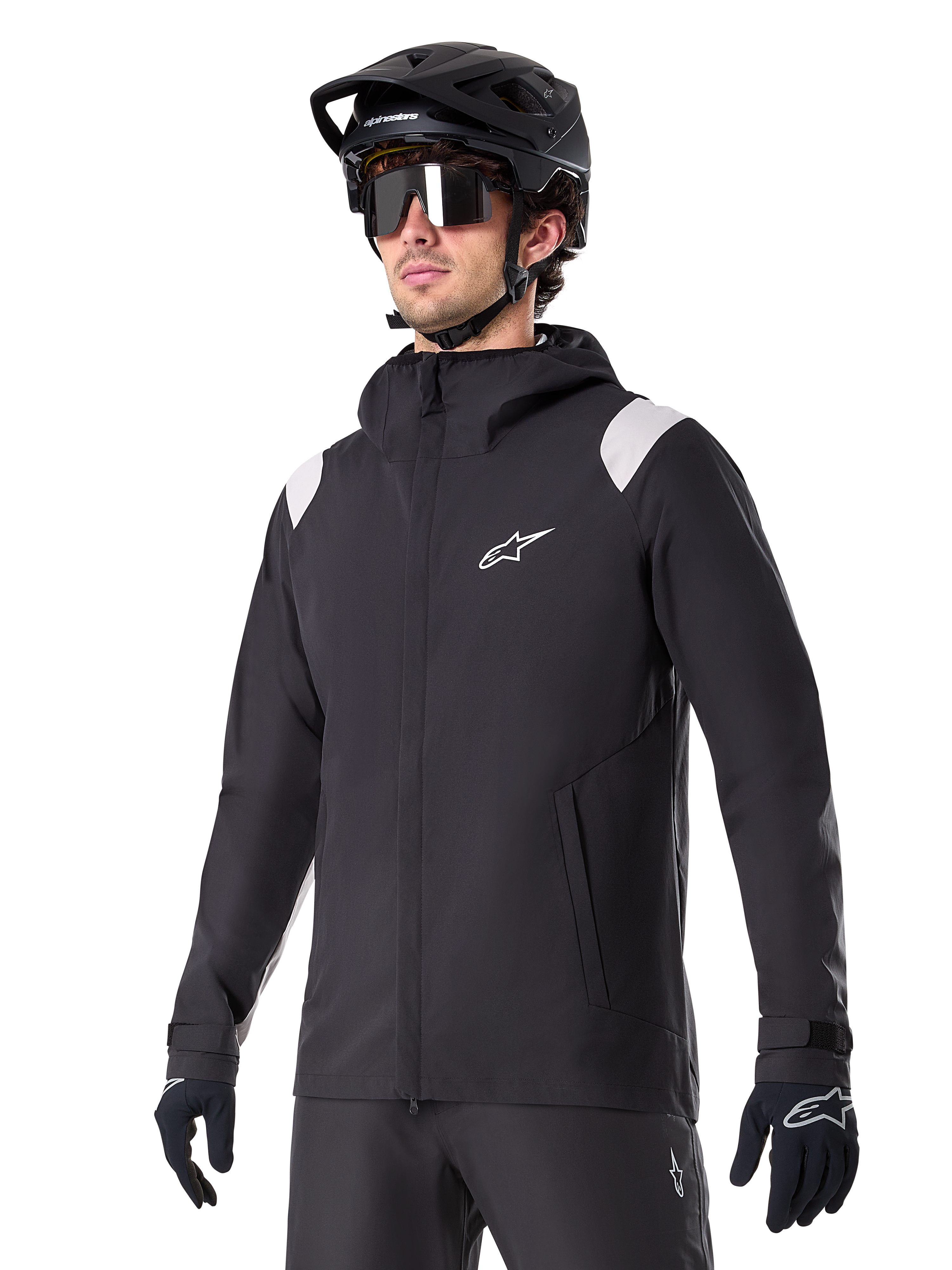 Alpinestars A-Dura Rain Jacket, giacca antipioggia da mountain bike, nera con inserti grigio chiaro sulle spalle, indossata da un ciclista con casco da MTB nero e occhiali da sole, logo bianco sul petto, costruzione impermeabile, coordinata con pantaloni e guanti neri per ciclismo fuoristrada
