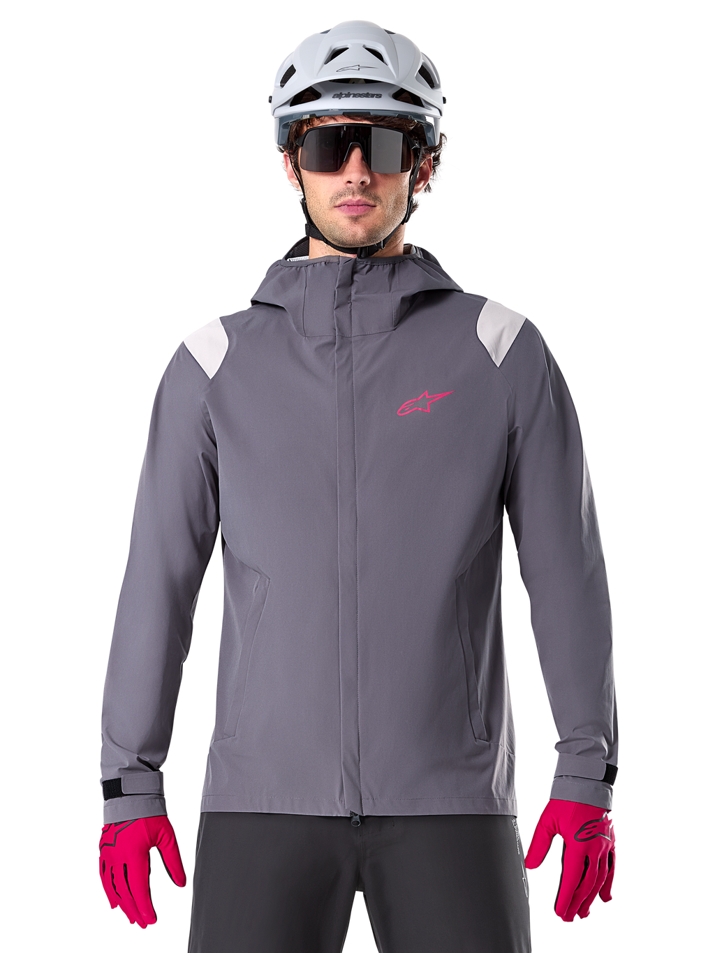 Alpinestars A-Dura Rain Jacket, giacca antipioggia da mountain bike, grigio Dark Titanium, design con cappuccio con logo Alpinestars rosa e inserti grigio chiaro sulle spalle, indossata con casco da MTB bianco e guanti rosa acceso, abbigliamento impermeabile per ciclismo fuoristrada