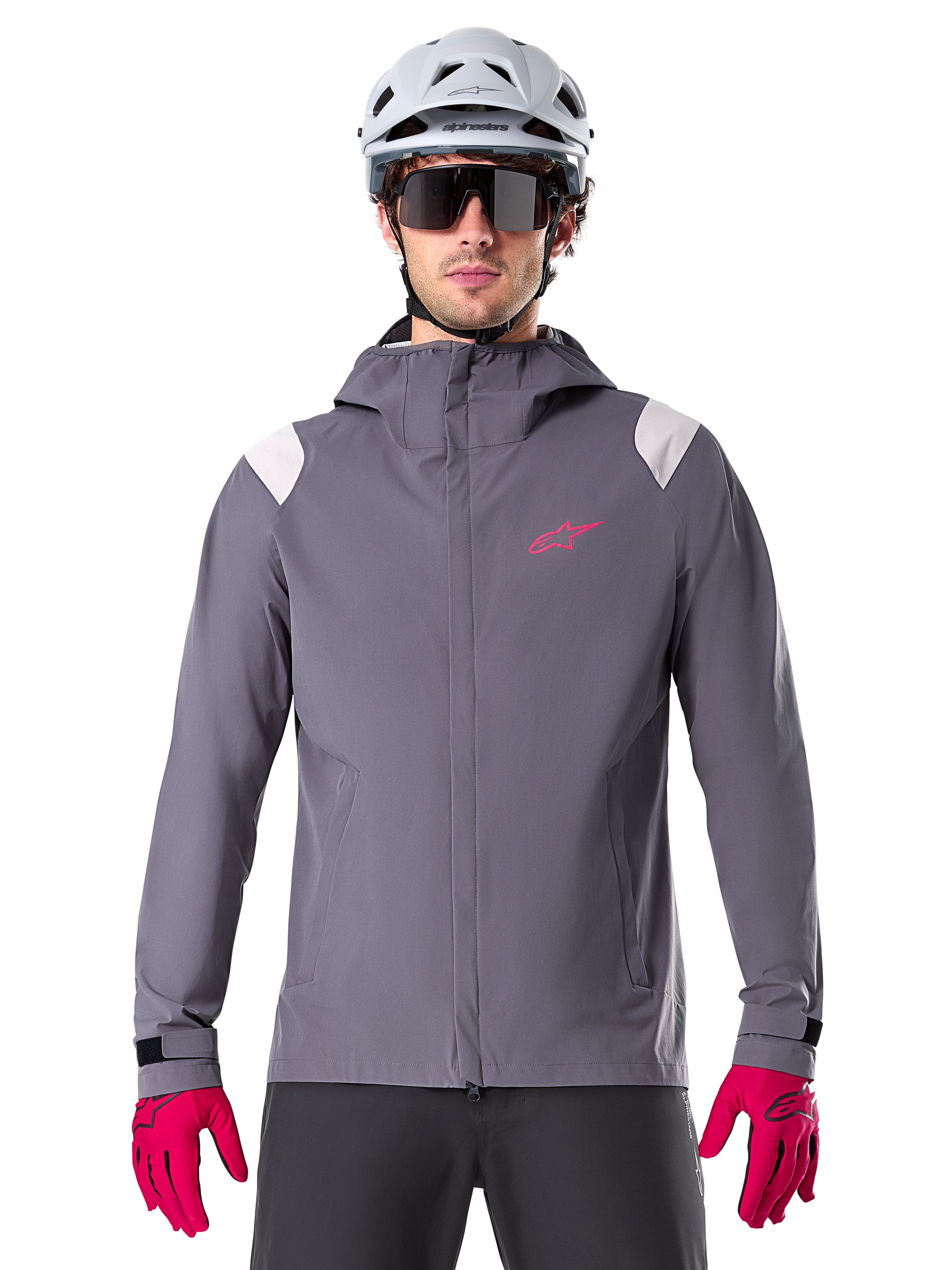 Alpinestars A-Dura Rain Jacket, giacca antipioggia da mountain bike, grigio Dark Titanium, design con cappuccio con logo Alpinestars rosa e inserti grigio chiaro sulle spalle, indossata con casco da MTB bianco e guanti rosa acceso, abbigliamento impermeabile per ciclismo fuoristrada