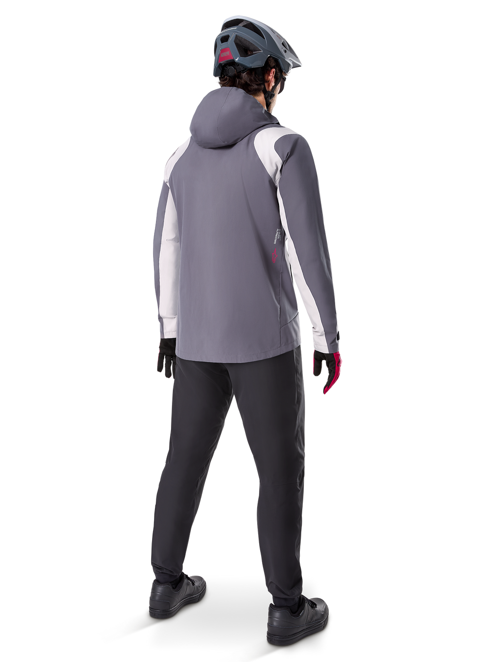 Giacca Antipioggia Alpinestars A-Dura, giacca da mountain bike, grigio titanio scuro con pannelli bianchi, vista posteriore del ciclista con casco grigio coordinato e pantaloni neri, abbigliamento tecnico outdoor per il maltempo
