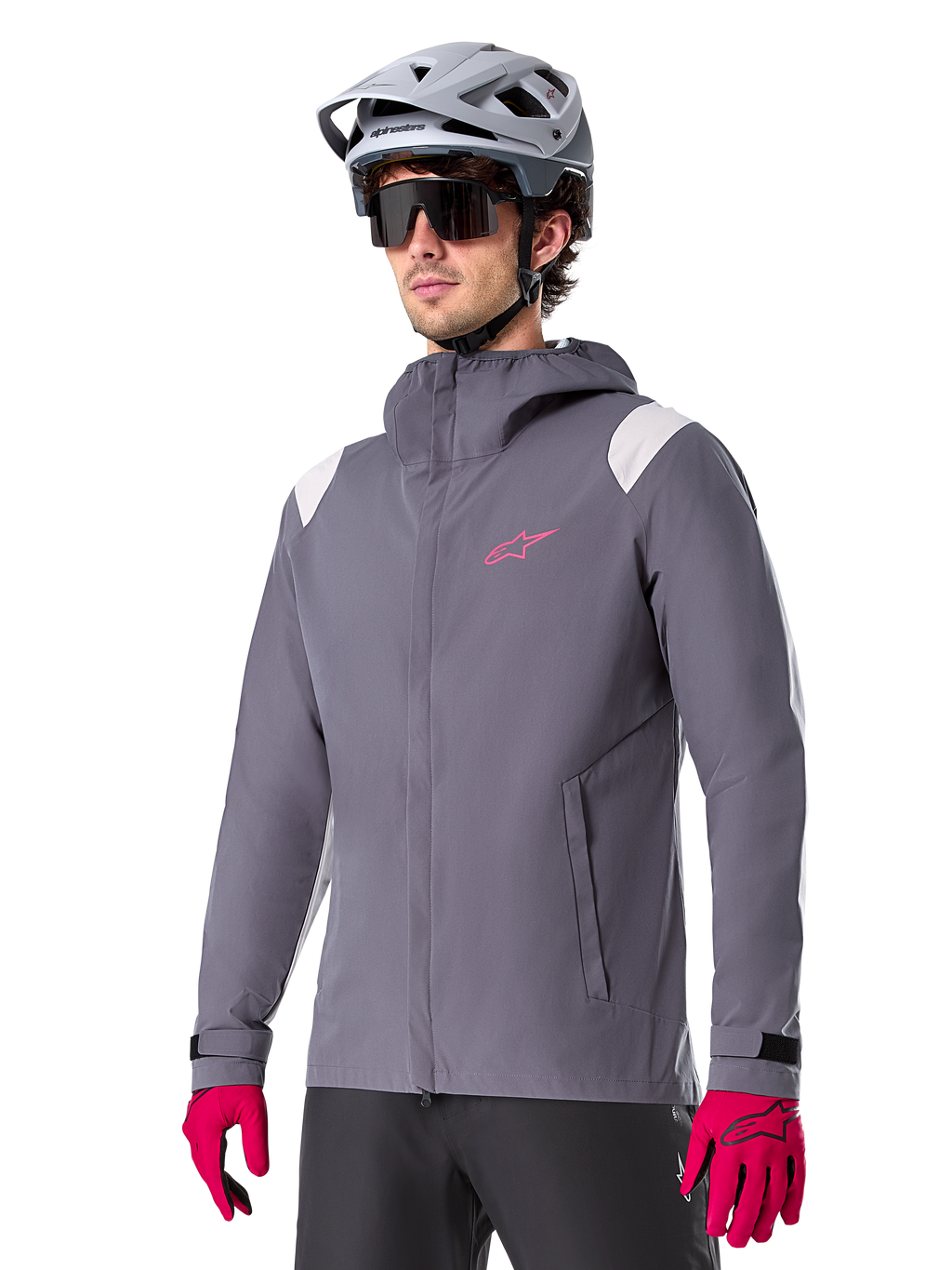 Alpinestars A-Dura Rain Jacket, giacca antipioggia da mountain bike, grigio titanio scuro con logo rosa e accenti bianchi sulle spalle, design con cappuccio e tasche anteriori, indossata con guanti rosa e casco da ciclismo grigio chiaro