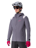 Alpinestars A-Dura Rain Jacket, giacca antipioggia da mountain bike, grigio titanio scuro con logo rosa e accenti bianchi sulle spalle, design con cappuccio e tasche anteriori, indossata con guanti rosa e casco da ciclismo grigio chiaro