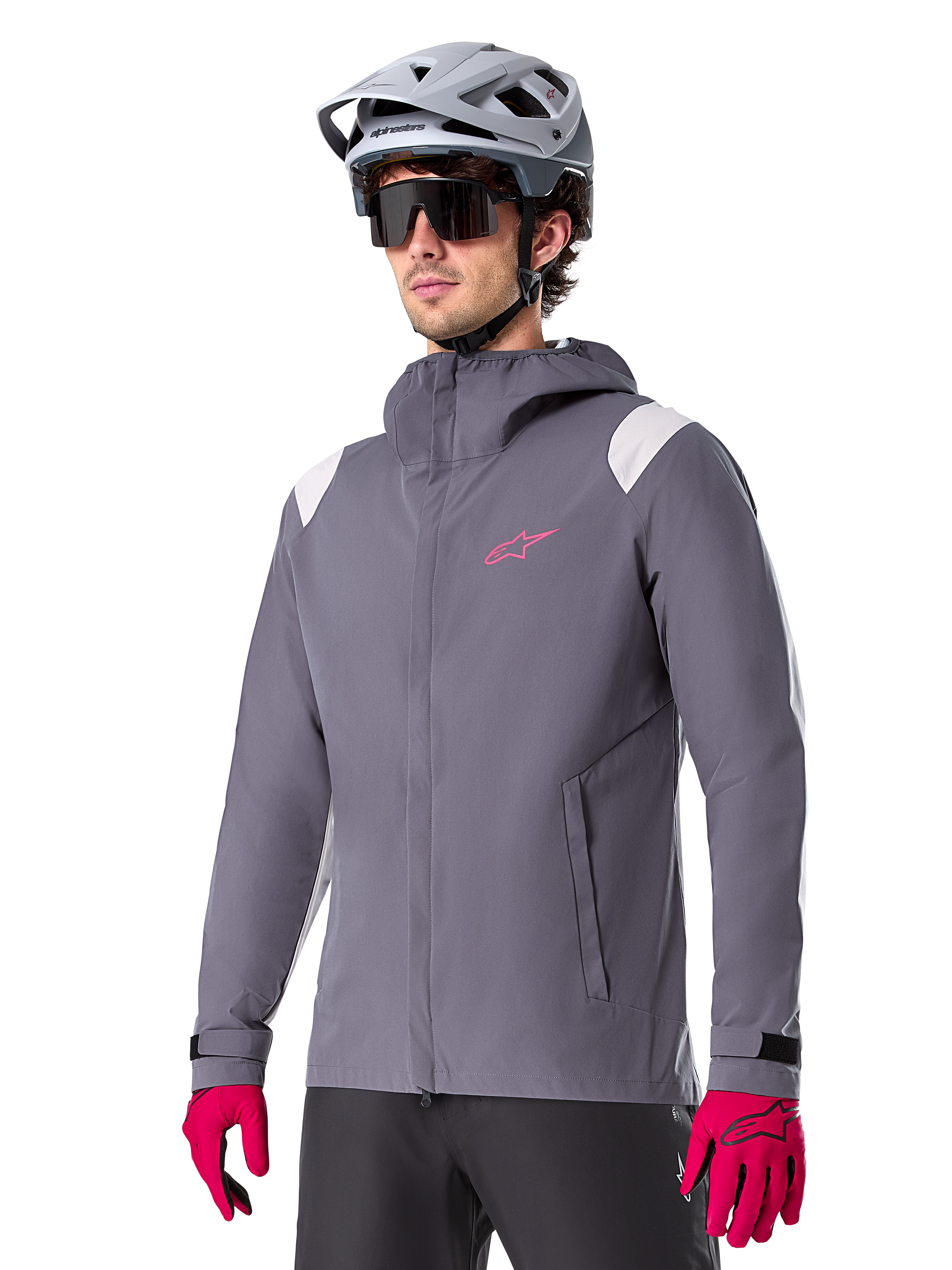 Alpinestars A-Dura Rain Jacket, giacca antipioggia da mountain bike, grigio titanio scuro con logo rosa e accenti bianchi sulle spalle, design con cappuccio e tasche anteriori, indossata con guanti rosa e casco da ciclismo grigio chiaro