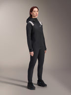 Donna che indossa la giacca antipioggia Alpinestars Stella A-Dura in nero, guscio MTB impermeabile a 2,5 strati con dettagli grigio chiaro sulle spalle, pantaloni neri e scarpe da ciclismo abbinati, ritratto in studio per abbigliamento tecnico da ciclismo
