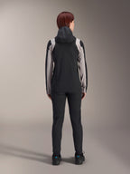 Alpinestars Stella A-Dura Rain Jacket, ciclista vista da dietro, nera con inserti grigio chiaro su maniche e spalle, cappuccio sollevato, indossata con pantaloni neri e scarpe da ciclismo, abbigliamento tecnico antipioggia per mountain bike