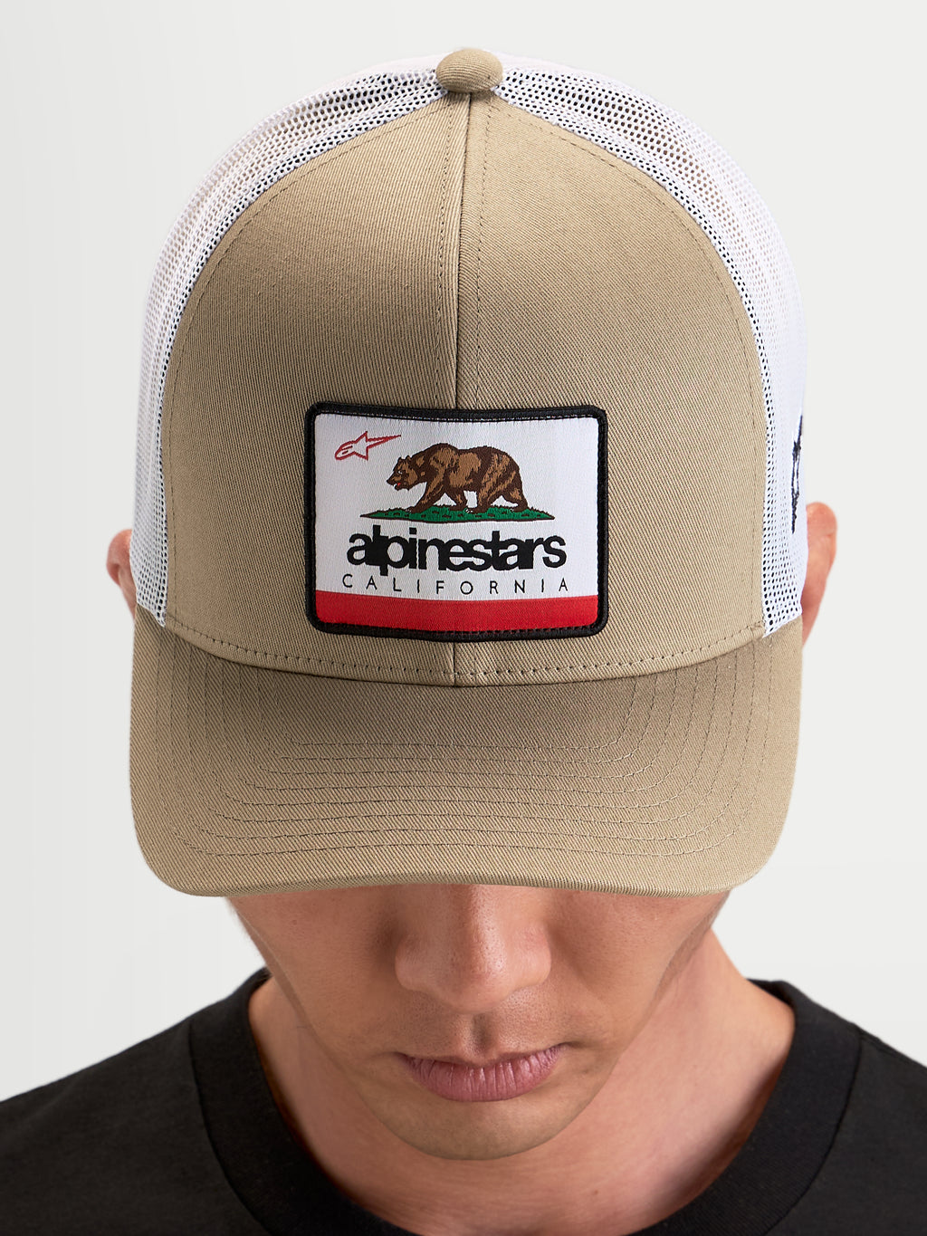 Alpinestars Cappello Cali 2.0, cappello trucker sportswear, kaki e bianco, con pannello frontale in twill strutturato, patch con orso della California e retro in rete traspirante indossato da un modello