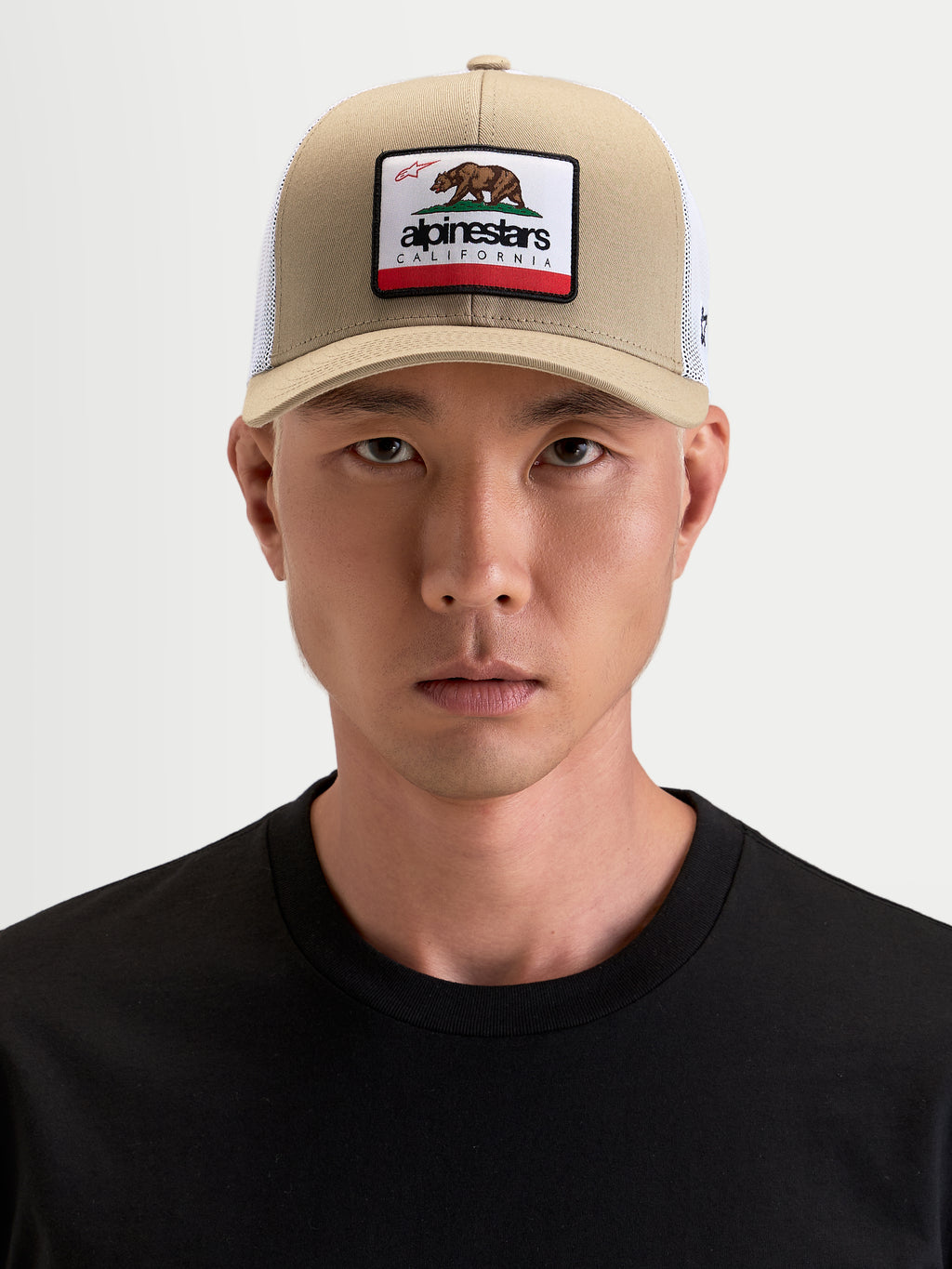 Alpinestars Cappello Cali 2.0, cappello trucker sportswear indossato da un modello, color cachi e bianco, con visiera curva e patch anteriore con orso californiano