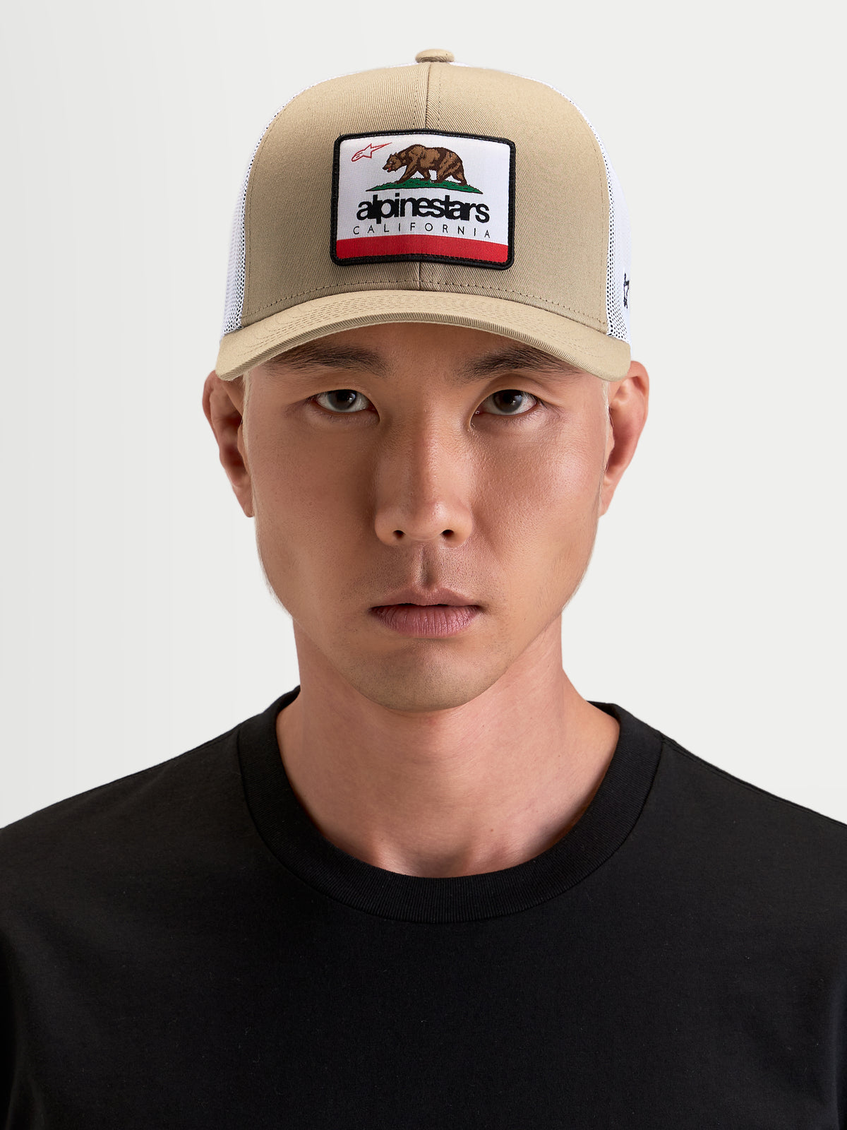 Alpinestars Cappello Cali 2.0, cappello trucker sportswear indossato da un modello, color cachi e bianco, con visiera curva e patch anteriore con orso californiano