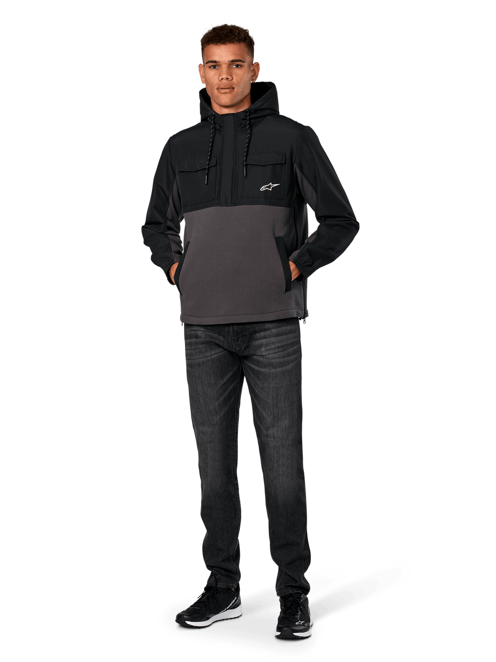 Giacca Hybrid Alpinestars Juncture, nero e gunmetal, felpa anorak con cappuccio in materiali misti, corpo in tela e pile con sovrapposizioni in ripstop, logo A-star bianco sul petto, cappuccio con coulisse, indossata da un modello con jeans scuri e sneakers nere, streetwear casual ispirato al motorsport
