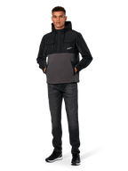 Giacca Hybrid Alpinestars Juncture, nero e gunmetal, felpa anorak con cappuccio in materiali misti, corpo in tela e pile con sovrapposizioni in ripstop, logo A-star bianco sul petto, cappuccio con coulisse, indossata da un modello con jeans scuri e sneakers nere, streetwear casual ispirato al motorsport