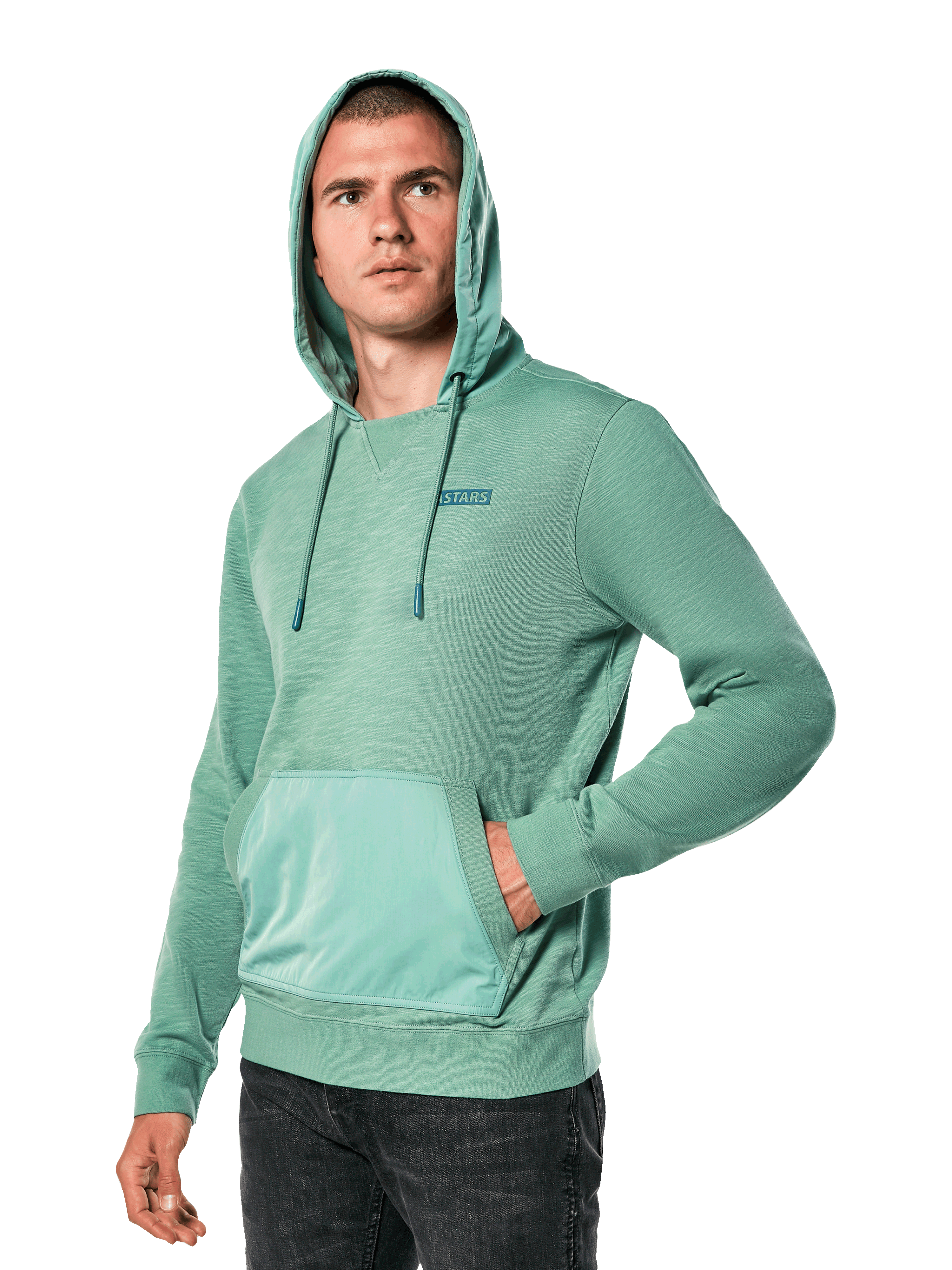 Alpinestars Rooted Hoodie, felpa in terry francese slub verde con cappuccio sovrapposto e tasca a marsupio, piccolo logo STARS sul petto, indossata da un modello con cappuccio alzato e mano in tasca, streetwear casual ispirato al motorsport