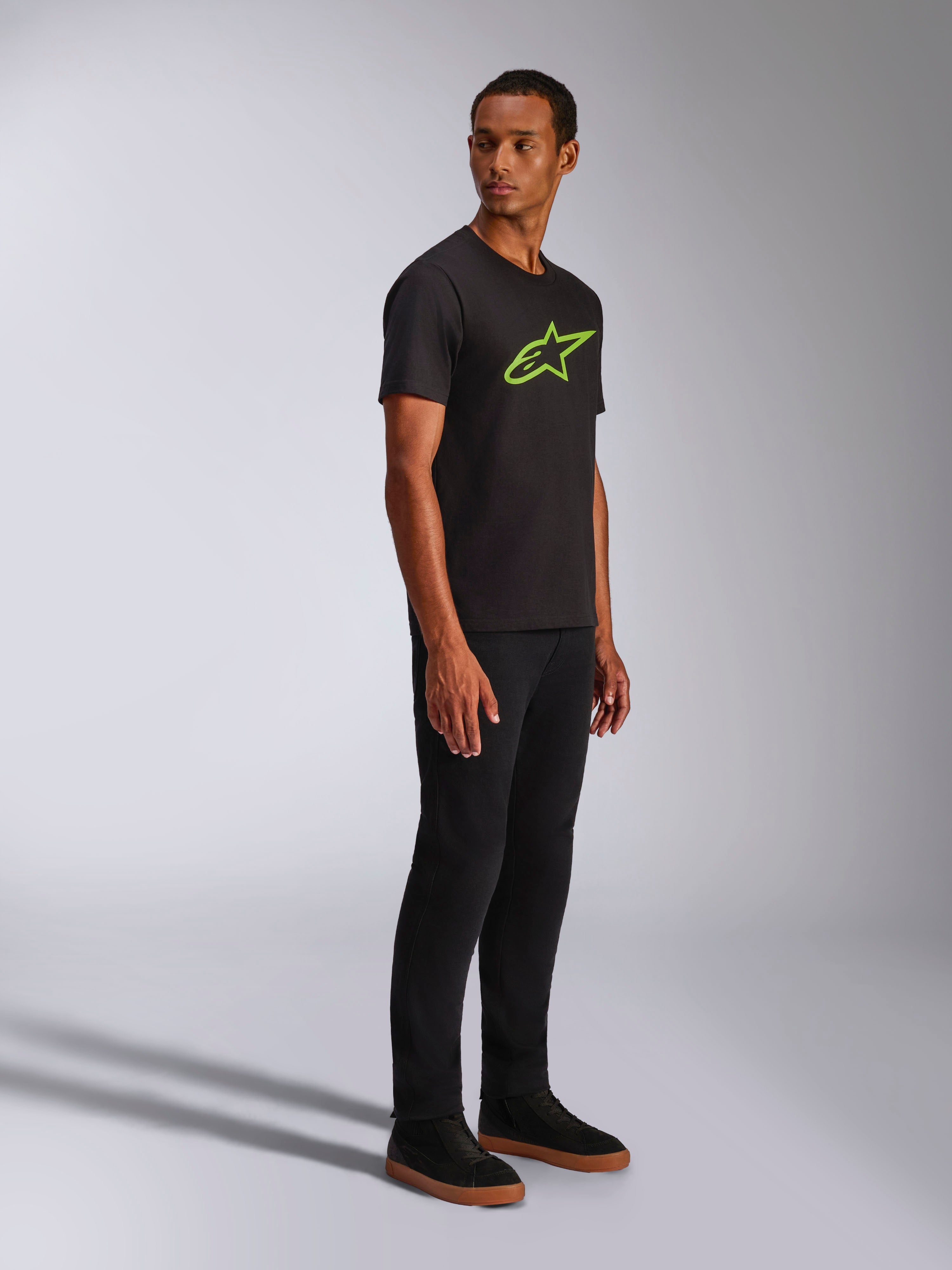 Alpinestars Ageless 2.0 CSF Tee, maglietta a maniche corte, nera con logo Alpinestars verde brillante, abbinata a pantaloni neri e sneakers, streetwear casual ispirato al motorsport