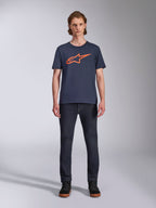 Alpinestars Ageless 2.0 CSF Tee, maglietta a maniche corte, blu navy con logo Alpinestars arancione, indossata da un modello con jeans scuri e sneakers, streetwear casual da motorsport